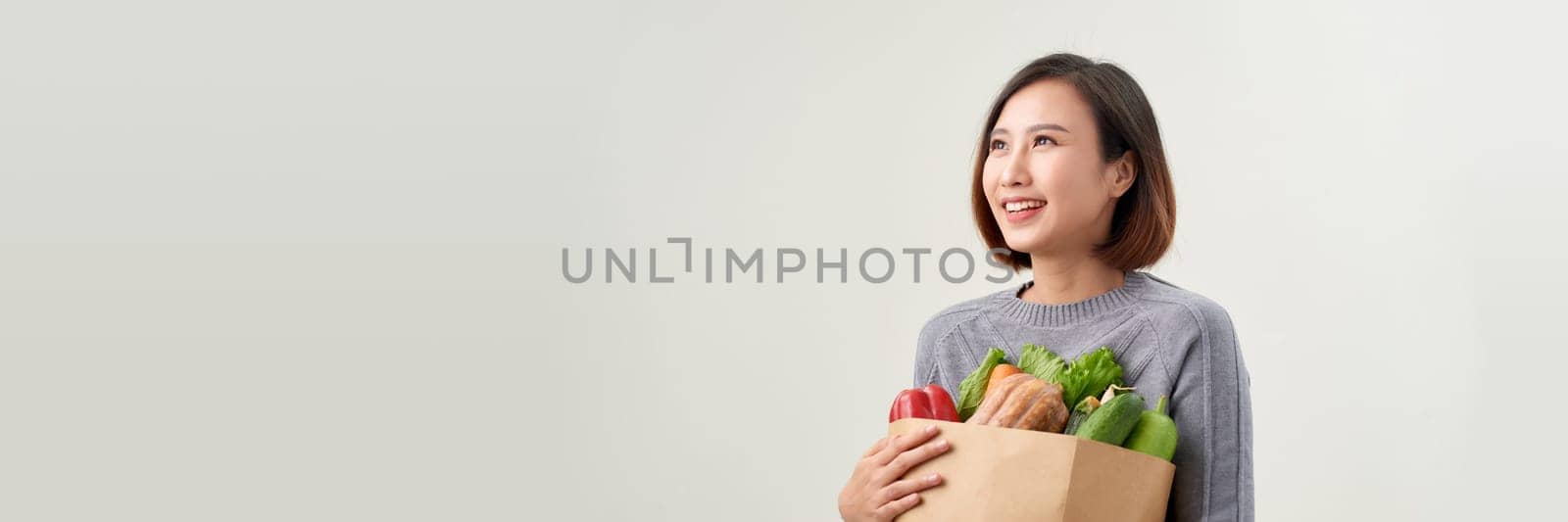 Happy woman holding paper bag full of fresh vegetable groceries isolated on white copy space background.