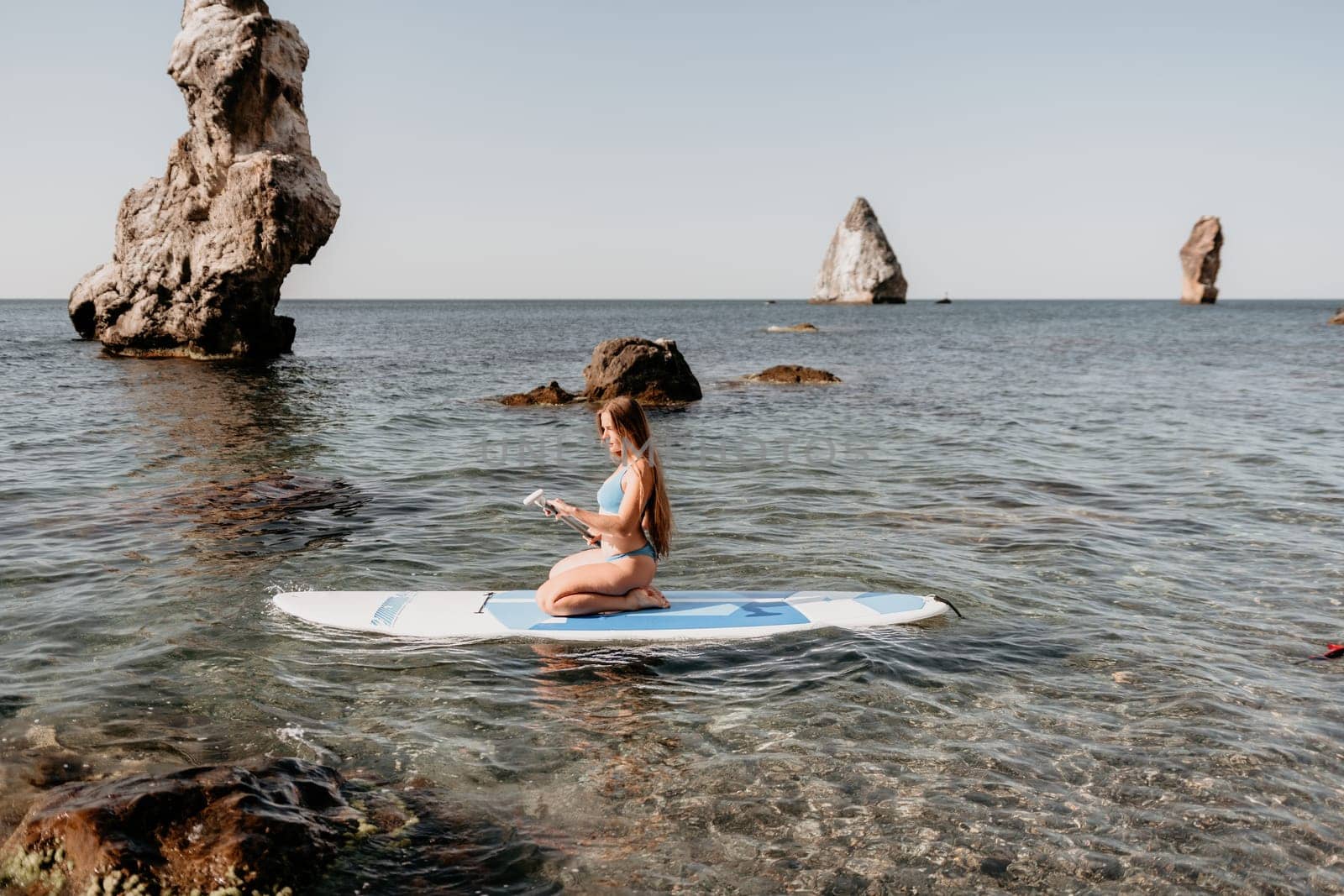 Woman sea sup. Close up portrait of happy young caucasian woman with long hair looking at camera and smiling. Cute woman portrait in a blue bikini posing on sup board in the sea by panophotograph