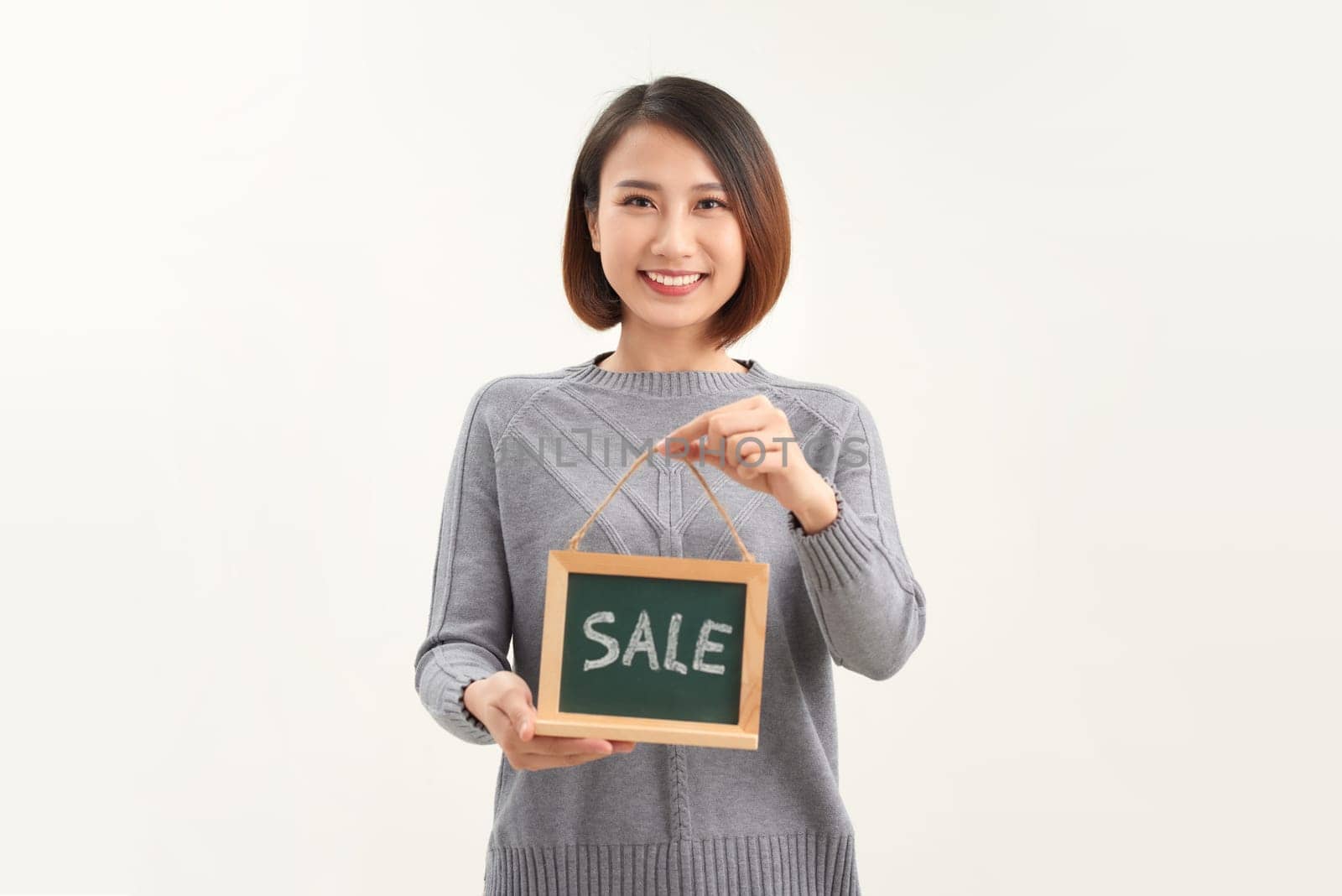 Young woman shop owner, wearing apron holding SALE word banner