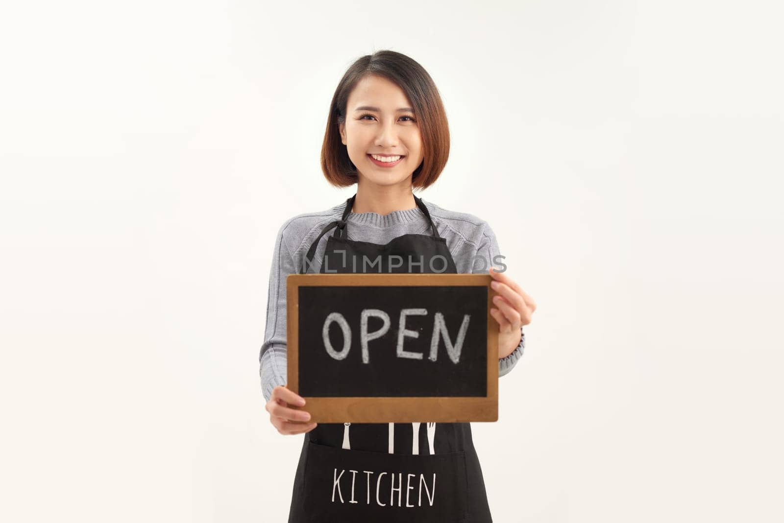 Young beautiful asian woman wearing apron holding open blackboard over isolated white background by makidotvn