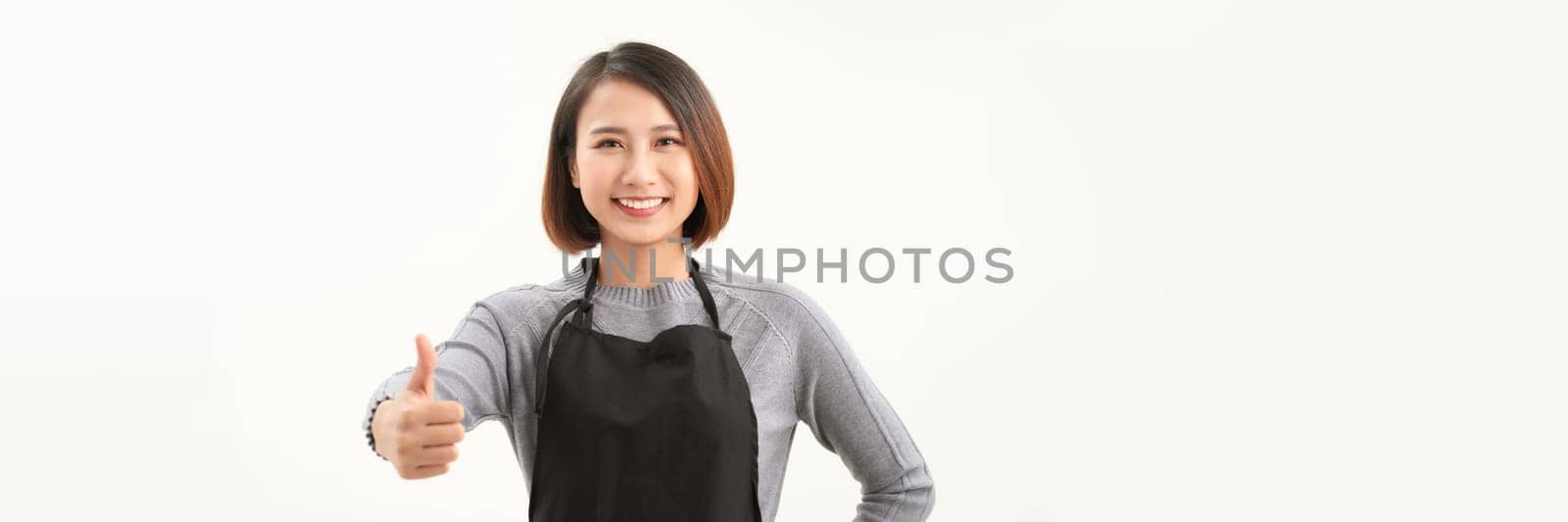 Cheerful young pretty female cafe staff in black apron show support or like gesture.