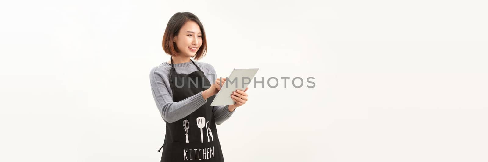 Friendly cute female barista in black apron smiling at camera, using digital tablet to manage cafe orders