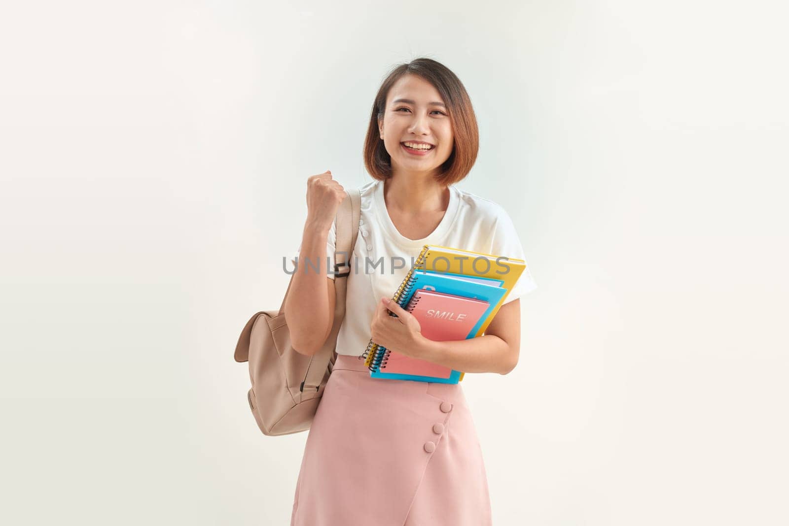 Portrait of smiling woman holding book and backpack leaning on white background by makidotvn