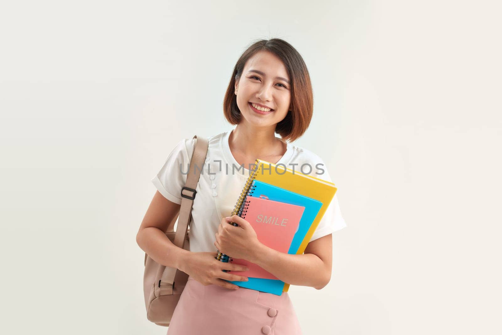 Cute student woman with backpack holds some documents and books over white background by makidotvn