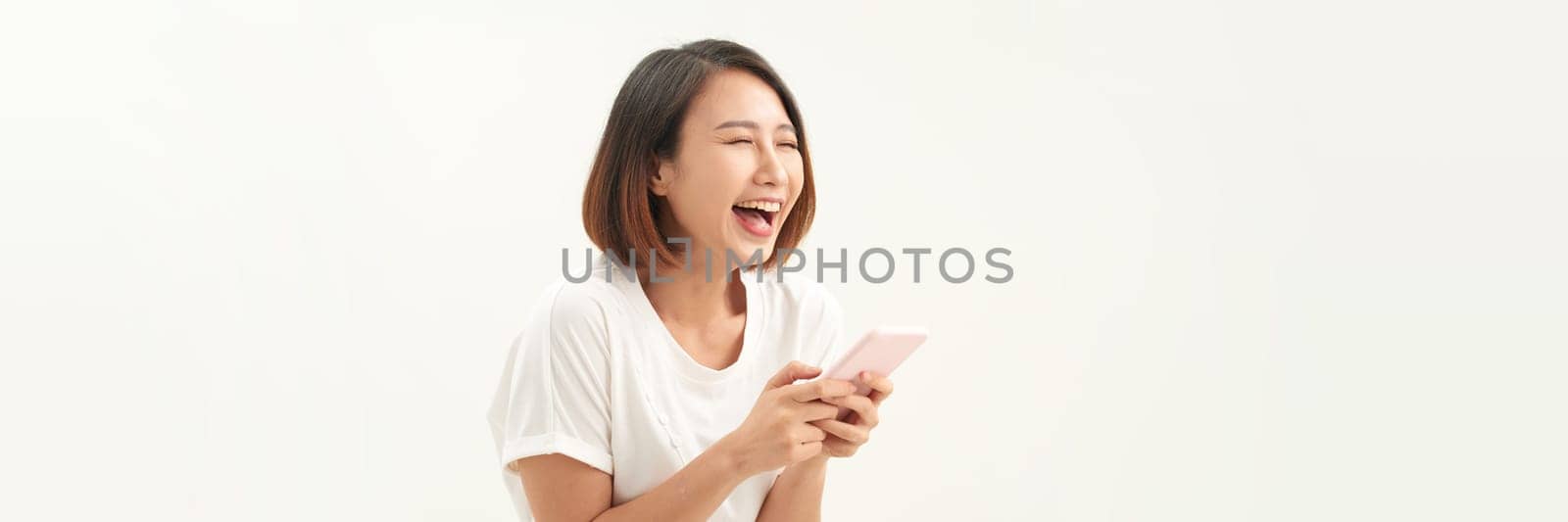 Portrait of excited asian woman using her mobile phone, isolated on white studio background