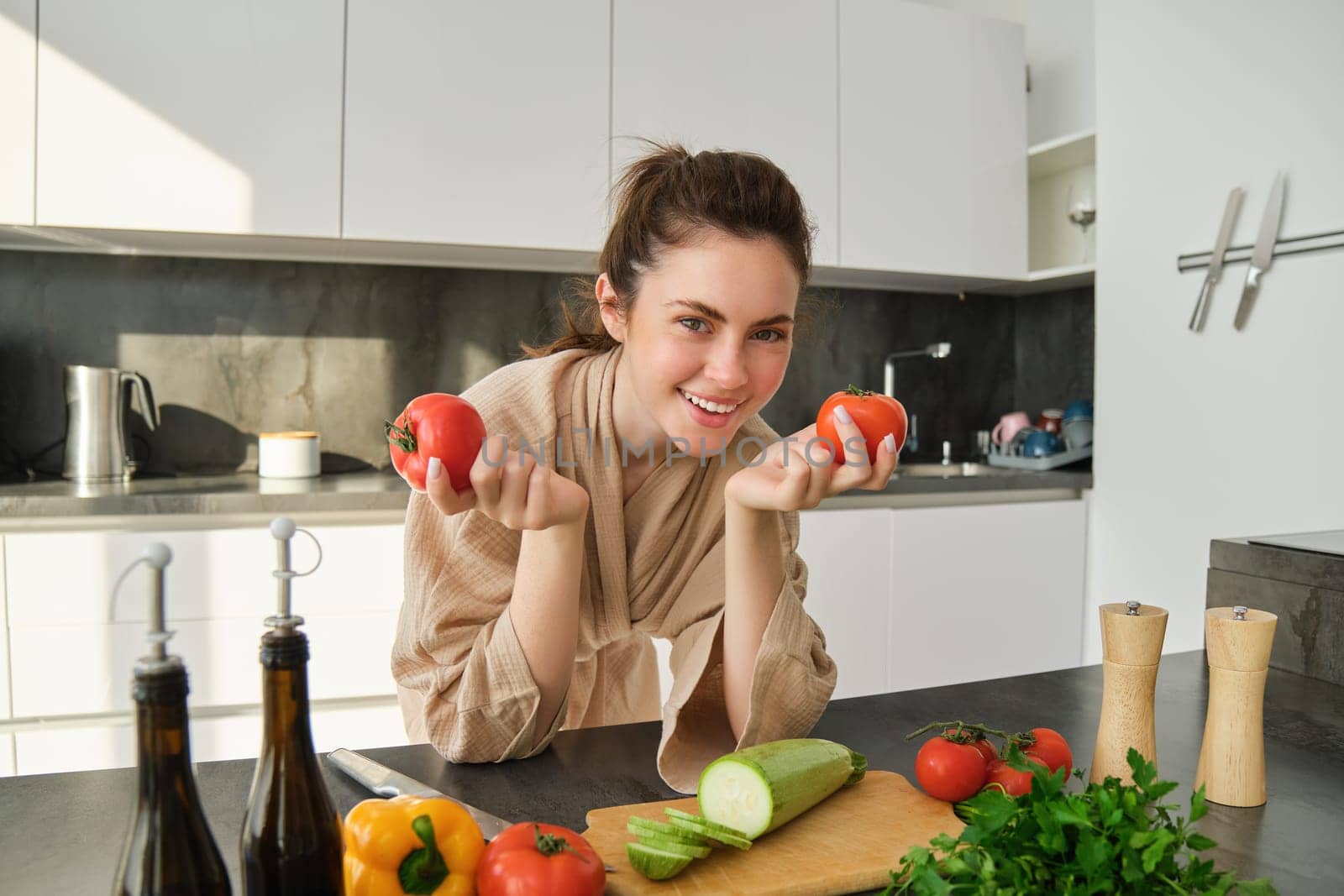 Portrait of woman cooking at home in the kitchen, holding tomatoes, preparing delicious fresh meal with vegetables, standing near chopping board by Benzoix