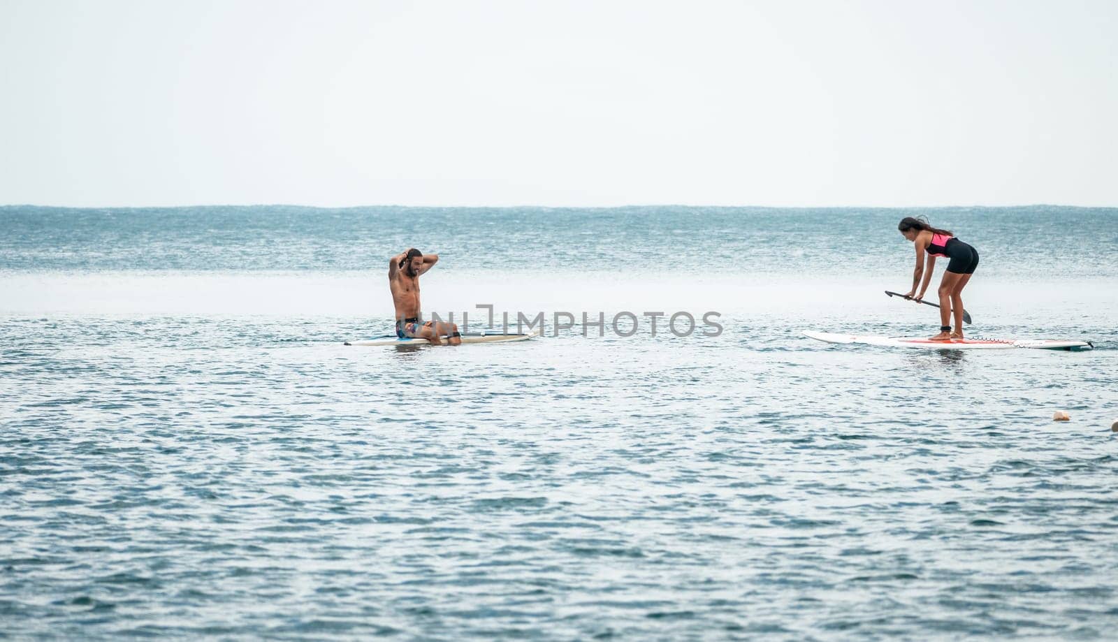 Sea woman and man on sup. Silhouette of happy young woman and man, surfing on SUP board, confident paddling through water surface. Idyllic sunset. Active lifestyle at sea or river