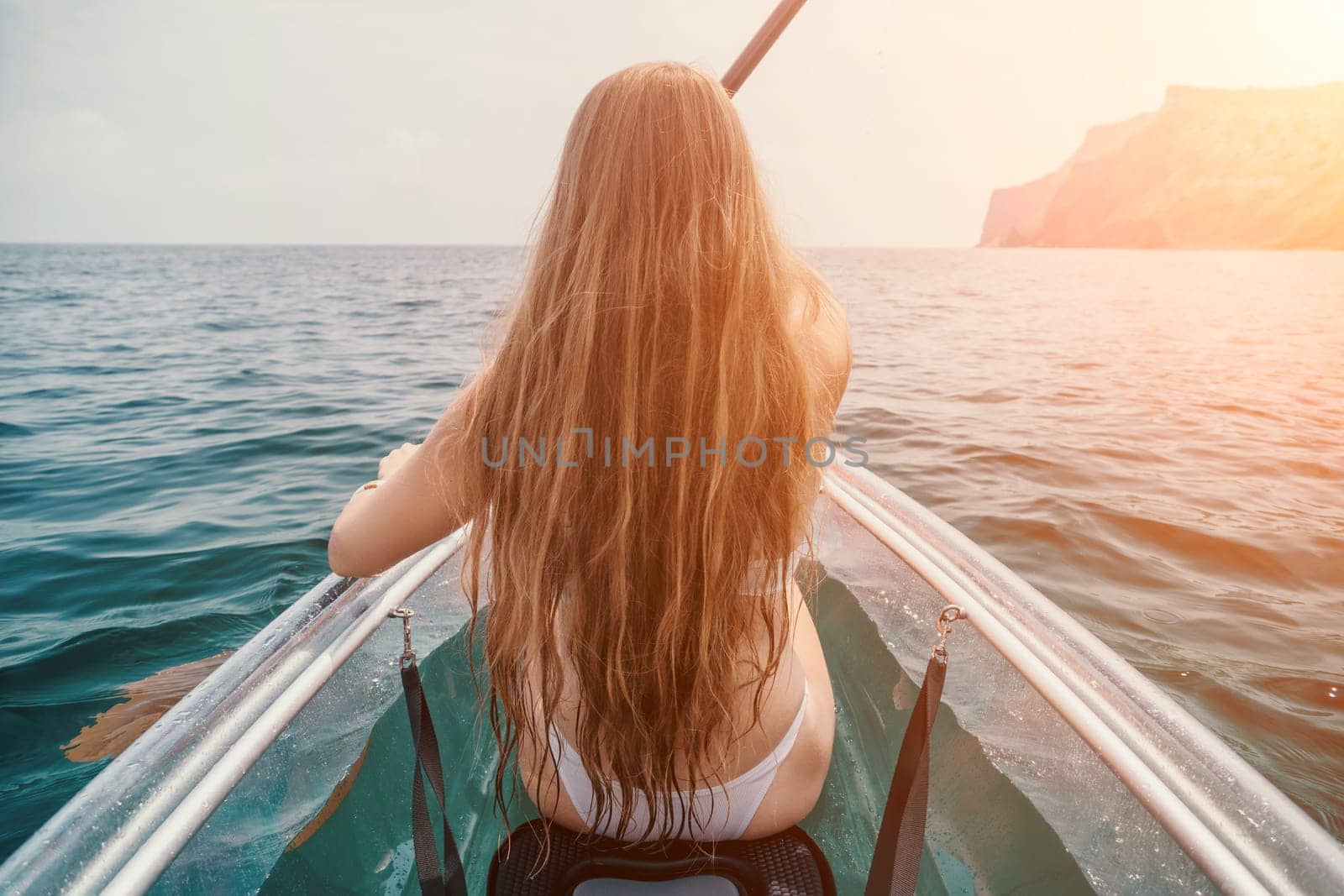 Woman in kayak back view. Happy young woman with long hair floating in transparent kayak on the crystal clear sea. Summer holiday vacation and cheerful female people relaxing having fun on the boat by panophotograph