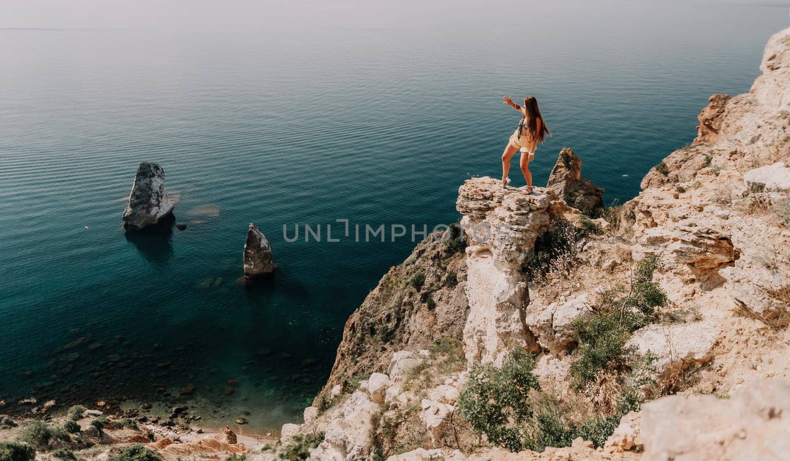 Woman travel sea. Happy tourist enjoy taking picture outdoors for memories. Woman traveler looks at the edge of the cliff on the sea bay of mountains, sharing travel adventure journey by panophotograph