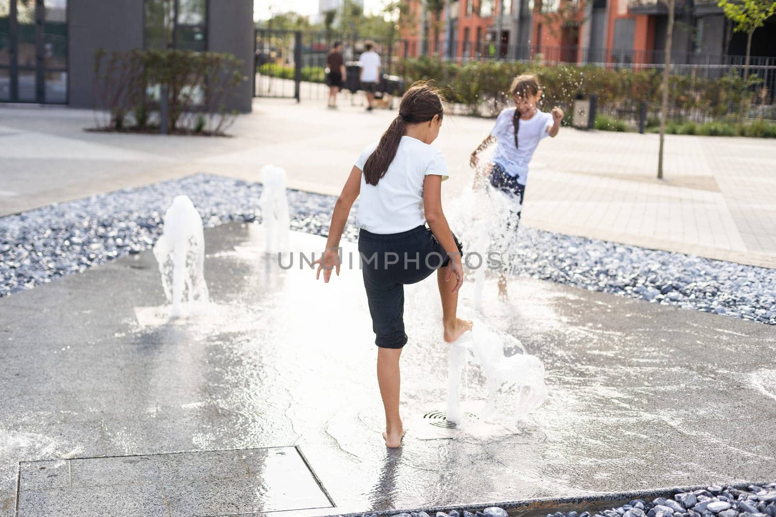 Cheerful young teen girl in city fountain, girl in wet clothes is having fun and enjoying the cool summer water, background city architecture. by Andelov13