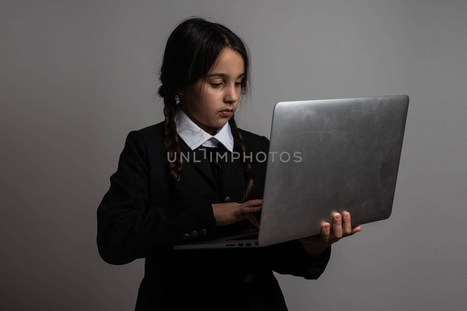 A girl with braids in a gothic style on a dark background with laptop.