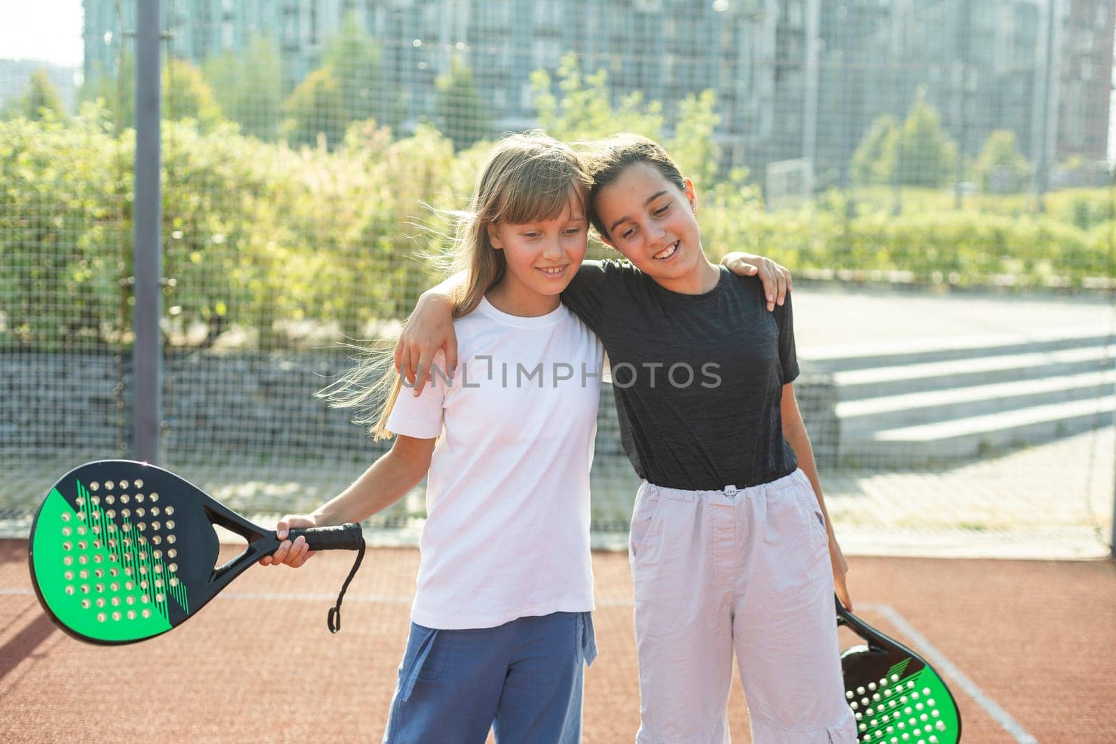 Kids and sports concept. Portrait of smiling girls posing outdoor on padel court with rackets and tennis balls by Andelov13