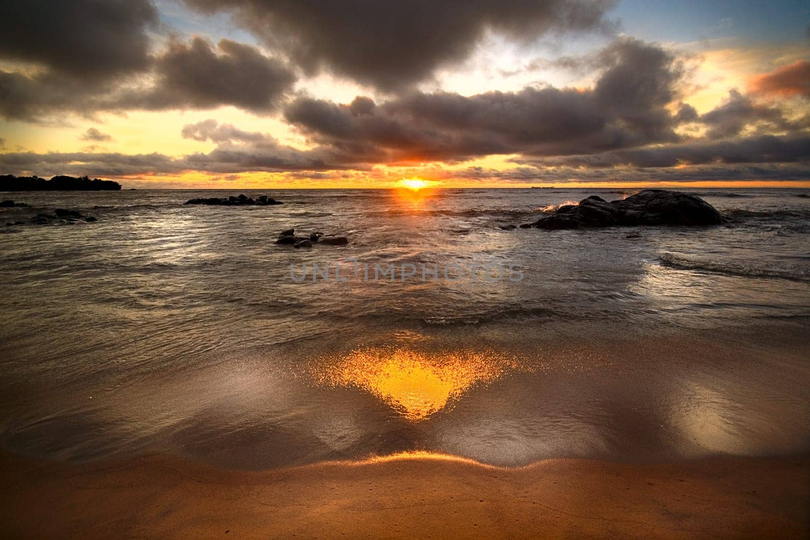 The sun sinks into the sea and sand