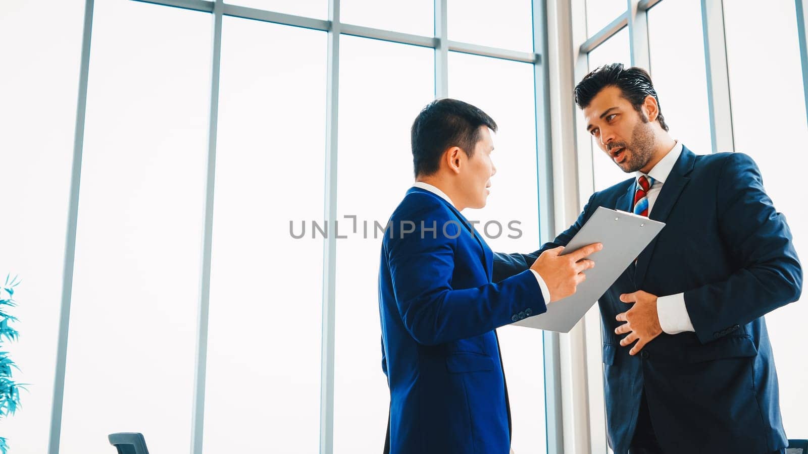 Two business people talk project strategy at office meeting room. Businessman discuss project planning with colleague at modern workplace while having conversation and advice on financial report. Jivy