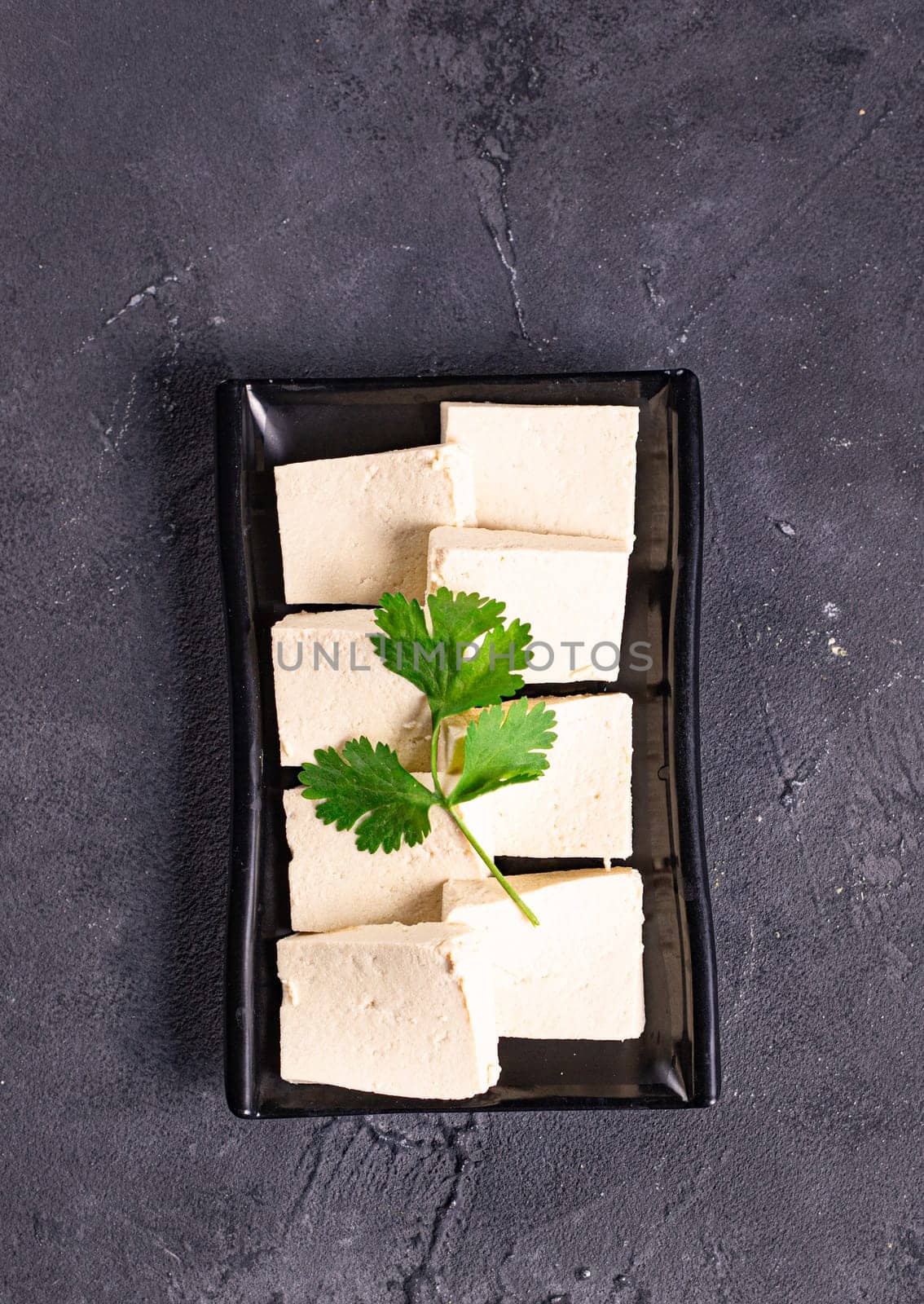 tofu slices with parsley on it on a black plate by tewolf