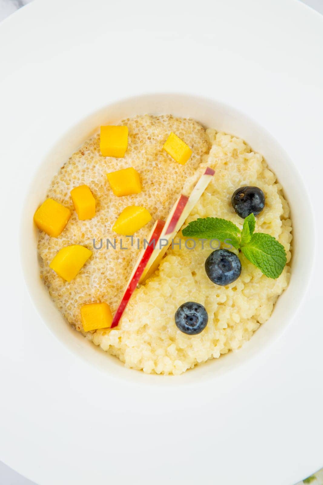 porridge with pieces of apple, mango, berries and mint in a white plate top view by tewolf