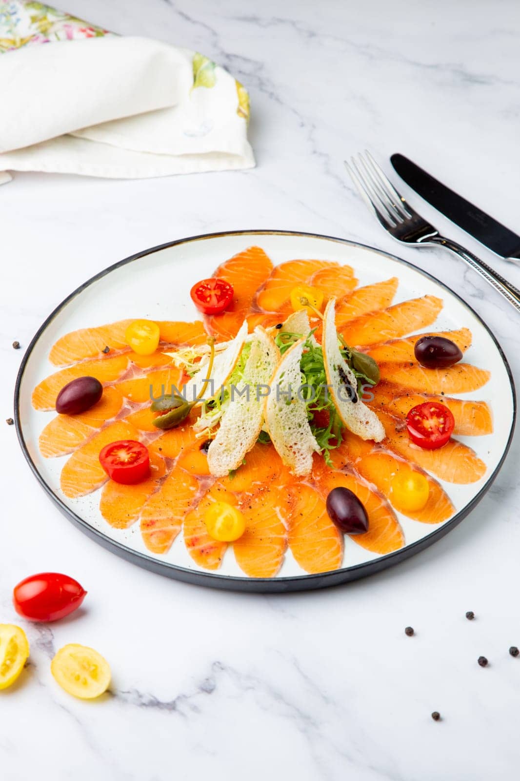 thinly sliced ​​pieces of smoked salmon with cherry tomatoes, olives and herbs on a white plate. view from above by tewolf