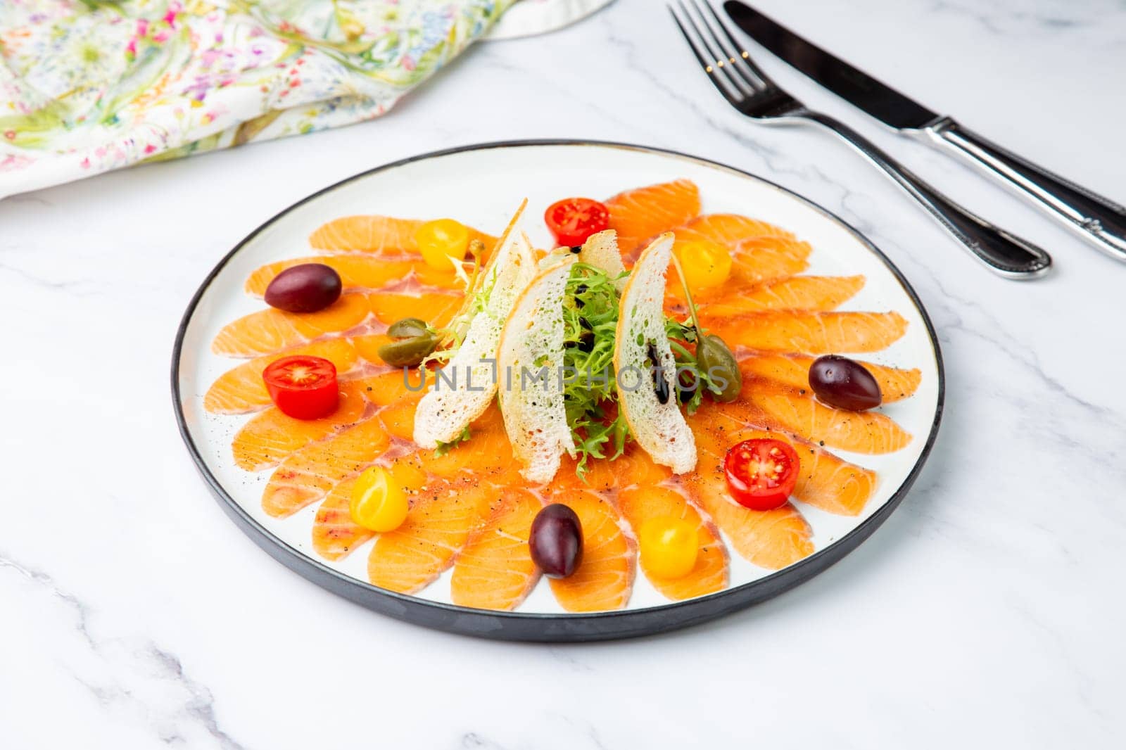 thinly sliced ​​pieces of smoked salmon with cherry tomatoes, olives and herbs on a white plate. view from above. High quality photo