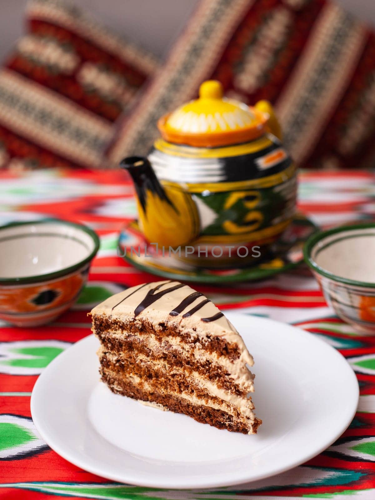 dessert chocolate cake with beige cream in oriental style on a rooftop with a teapot and a cup for tea. by tewolf