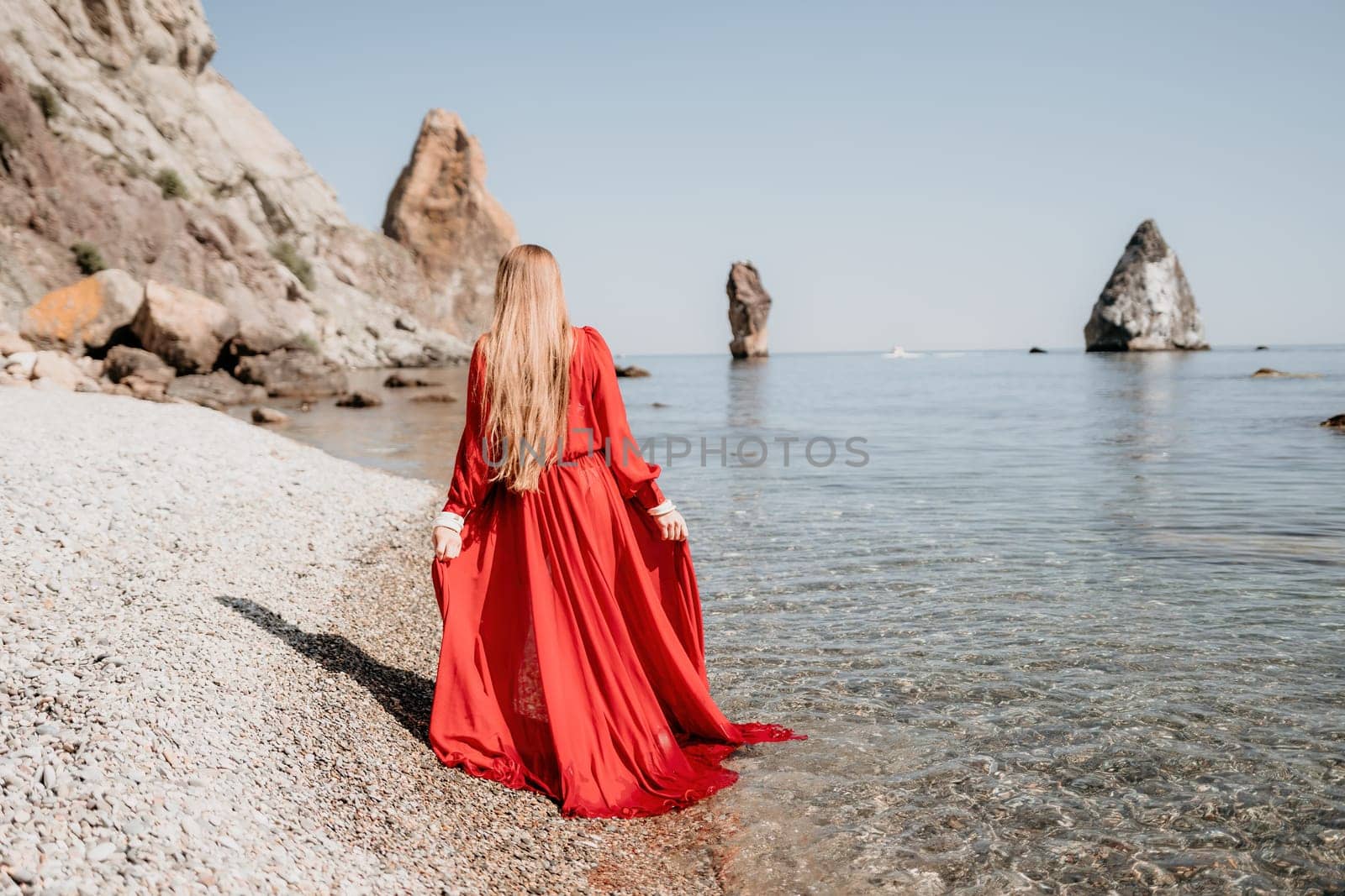 Woman travel sea. Happy tourist in red dress enjoy taking picture outdoors for memories. Woman traveler posing on the rock at sea bay surrounded by volcanic mountains, sharing travel adventure journey by panophotograph