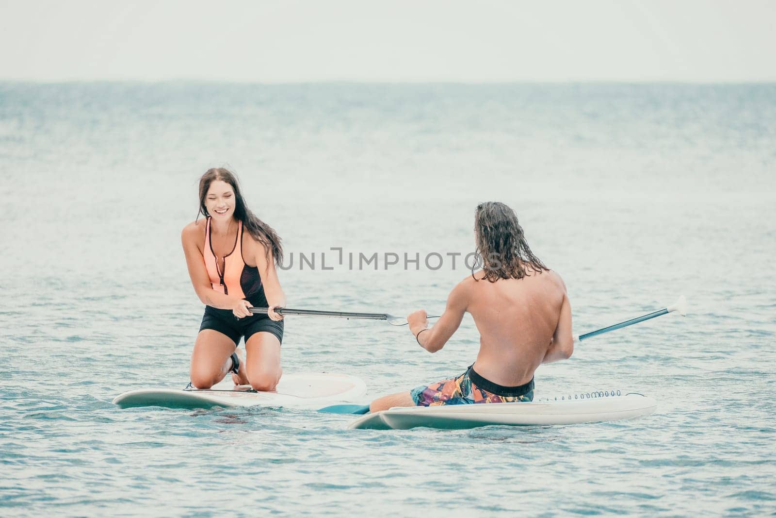 Sea woman and man on sup. Silhouette of happy young woman and man, surfing on SUP board, confident paddling through water surface. Idyllic sunset. Active lifestyle at sea or river