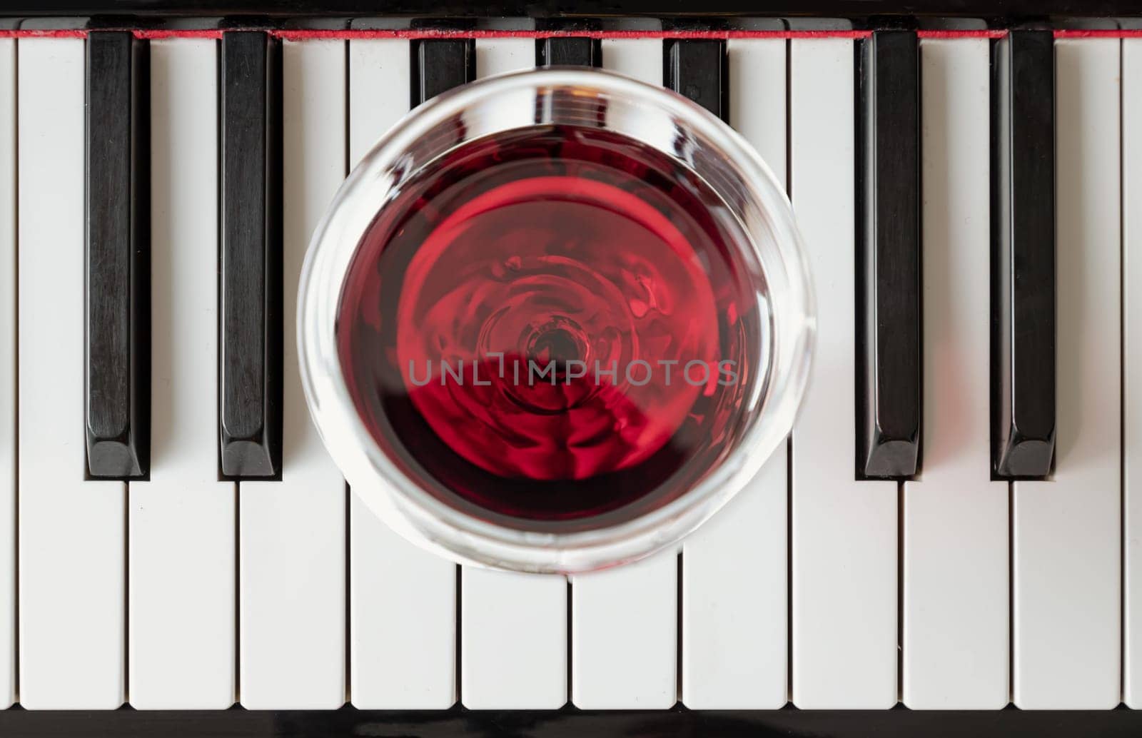Glass of red wine on piano keyboard. Music and wine concept, Top view, Space for text, Selective focus.