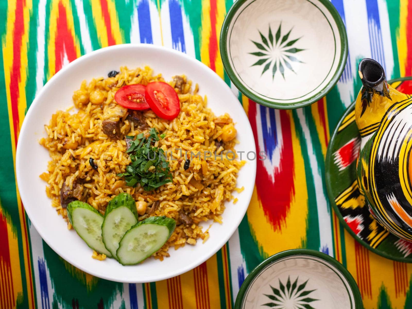 National Uzbek pilaf with meat on the table in the Uzbek style.on a table with a teapot and a cup for tea. by tewolf