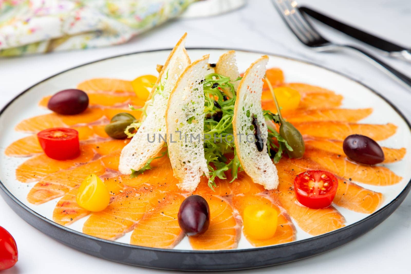 thinly sliced ​​pieces of smoked salmon with cherry tomatoes, olives and herbs on a white plate. view from above by tewolf