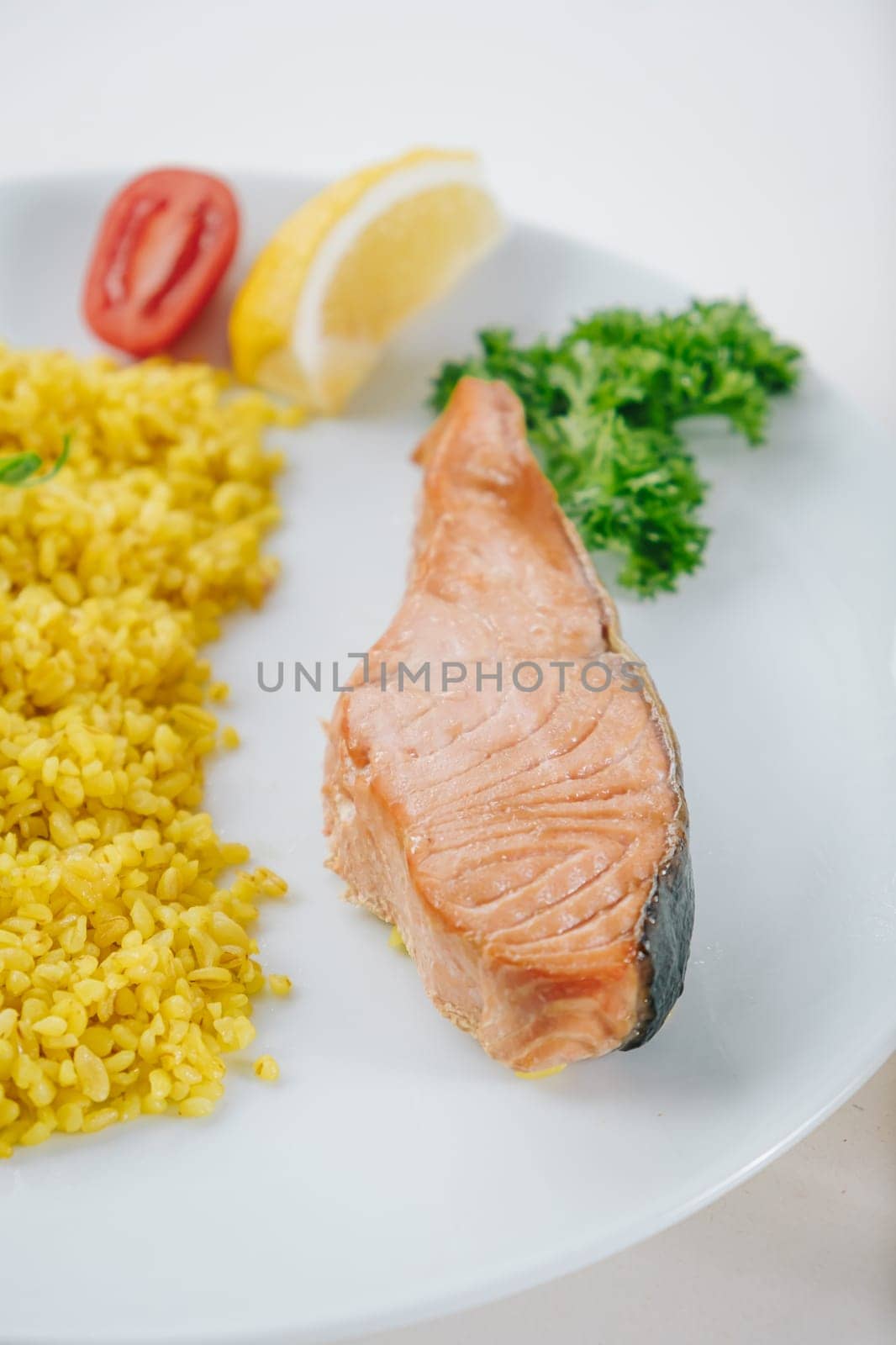 proper nutrition, daily diet, weight loss. greens, tomatoes, salmon steak with lemon and couscous garnish on a plate.