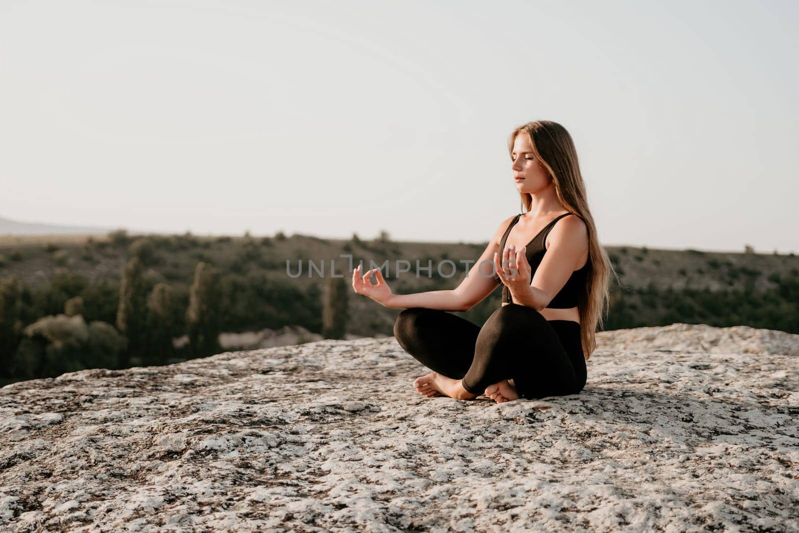 Fitness woman. Well looking middle aged woman with long hair, fitness instructor in leggings and tops doing stretching and pilates on the rock near forest. Female fitness yoga routine concept. by panophotograph