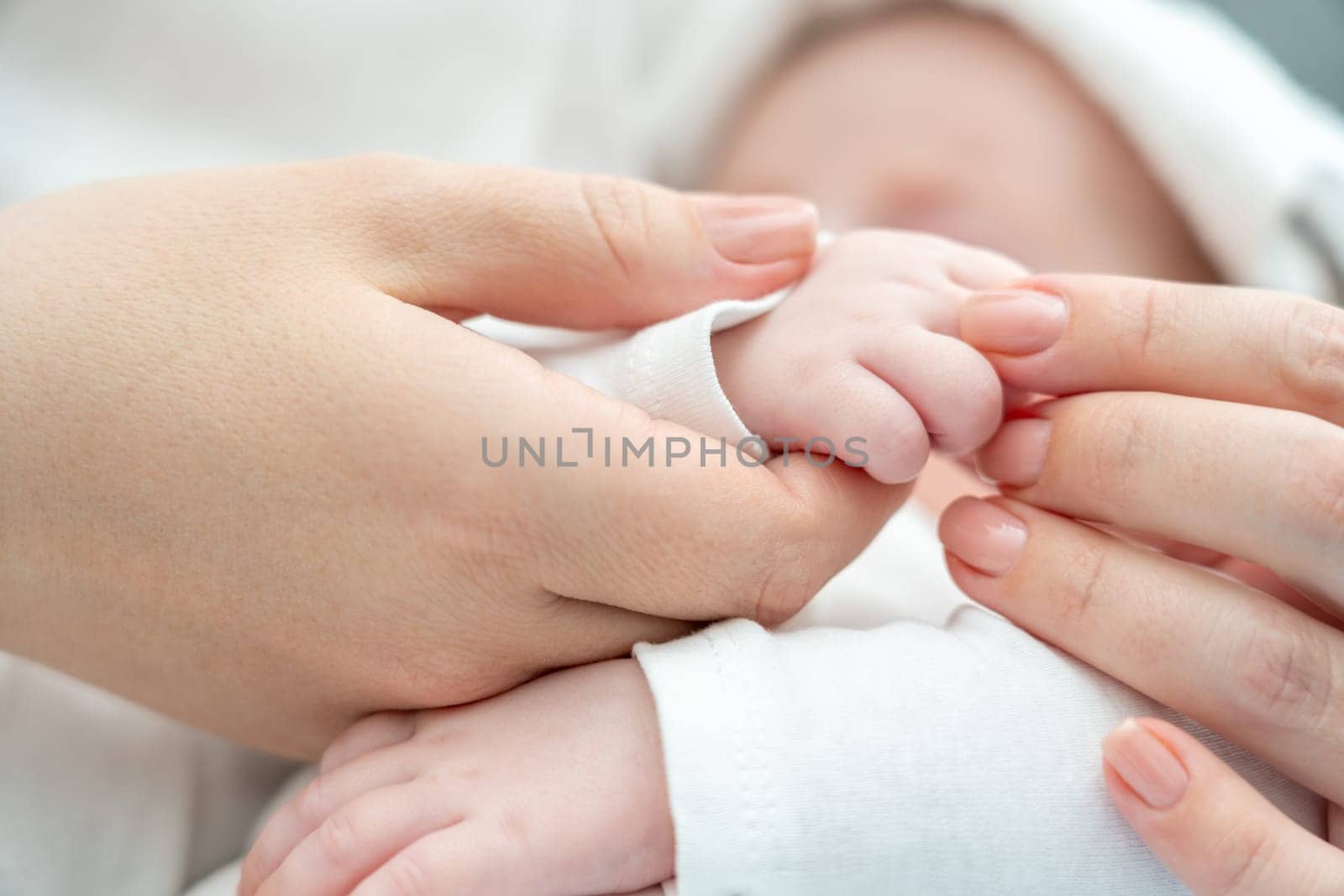 Close-up captures the fragile moment of an unwell newborn baby holding onto mother's finger, with a wet towel on the brow