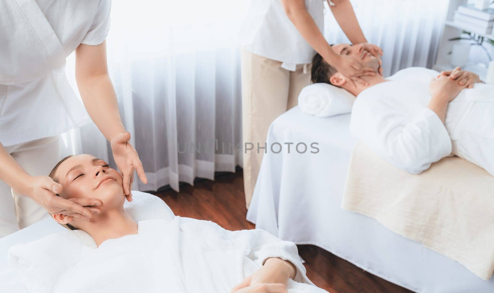 Caucasian couple enjoying relaxing anti-stress head massage and pampering facial beauty skin recreation leisure in dayspa modern light ambient at luxury resort or hotel spa salon. Quiescent