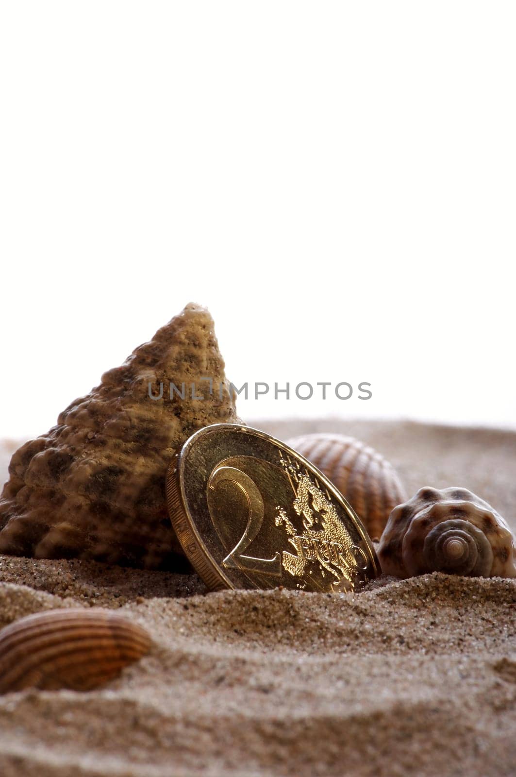 golden shiny 2 Euro piece with sand and shells as symbolism for holiday pay / holiday fund