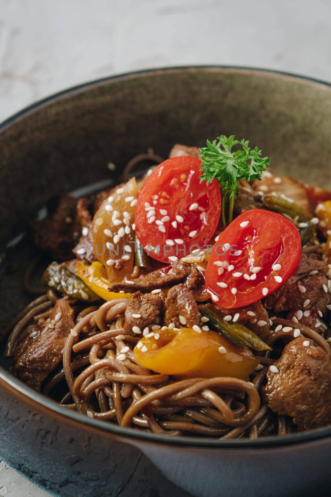 noodles with beef, vegetables, cherry tomatoes and sesame sauce in a deep plate side view by tewolf