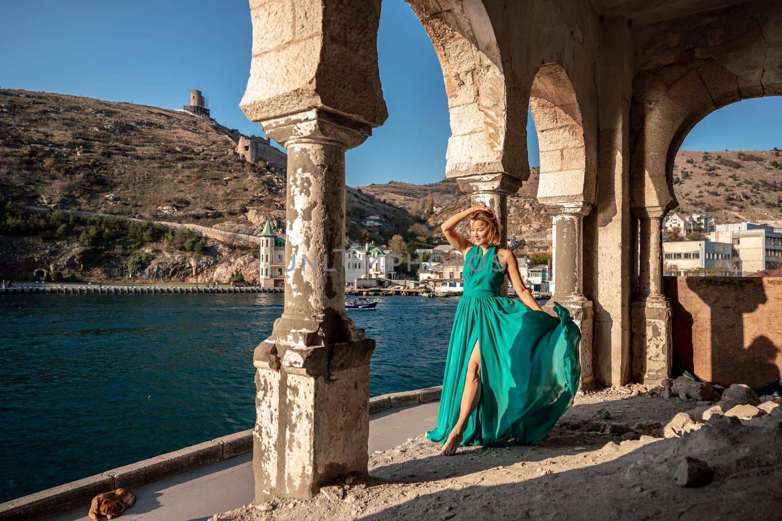 Woman dress sea columns. Rear view of a happy blonde woman in a long mint dress posing against the backdrop of the sea in an old building with columns. by Matiunina