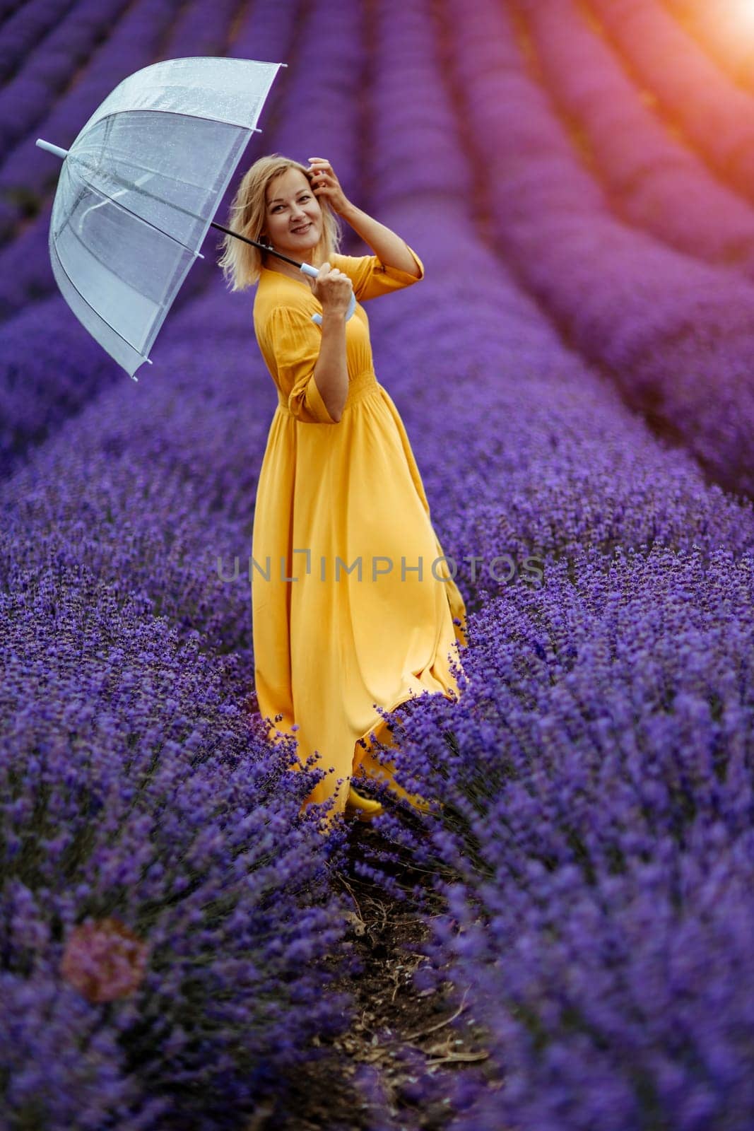 Woman lavender field. A middle-aged woman in a lavender field walks under an umbrella on a rainy day and enjoys aromatherapy. Aromatherapy concept, lavender oil, photo session in lavender by Matiunina