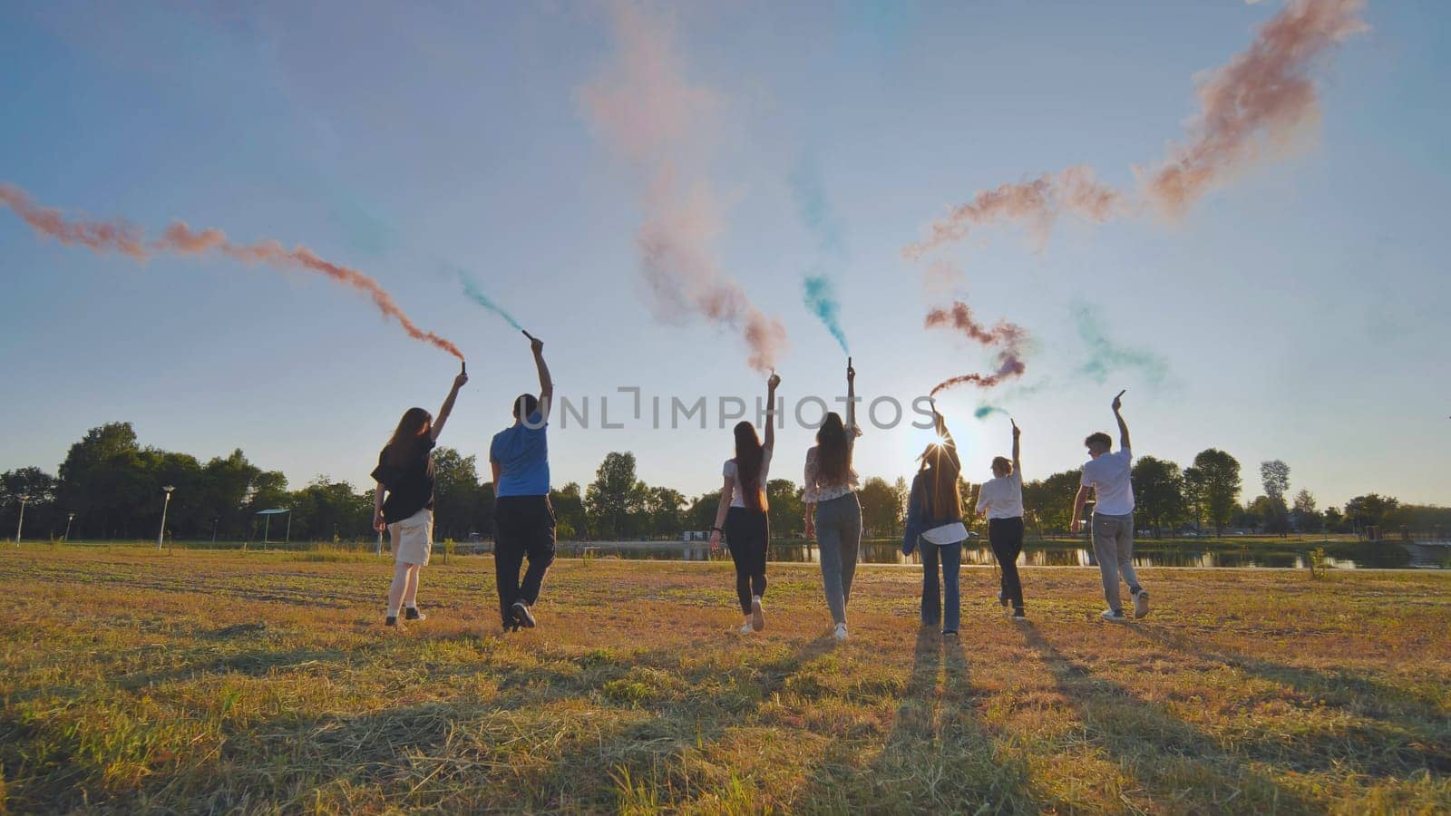 A group of friends spraying multi-colored smoke at sunset. by DovidPro