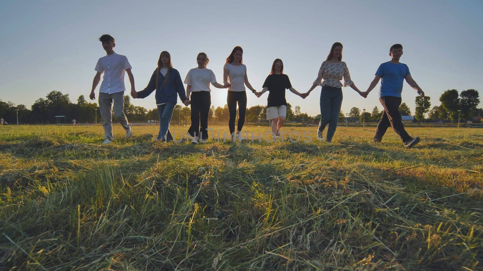 Friends at sunset holding hands walking against the backdrop of the setting sun