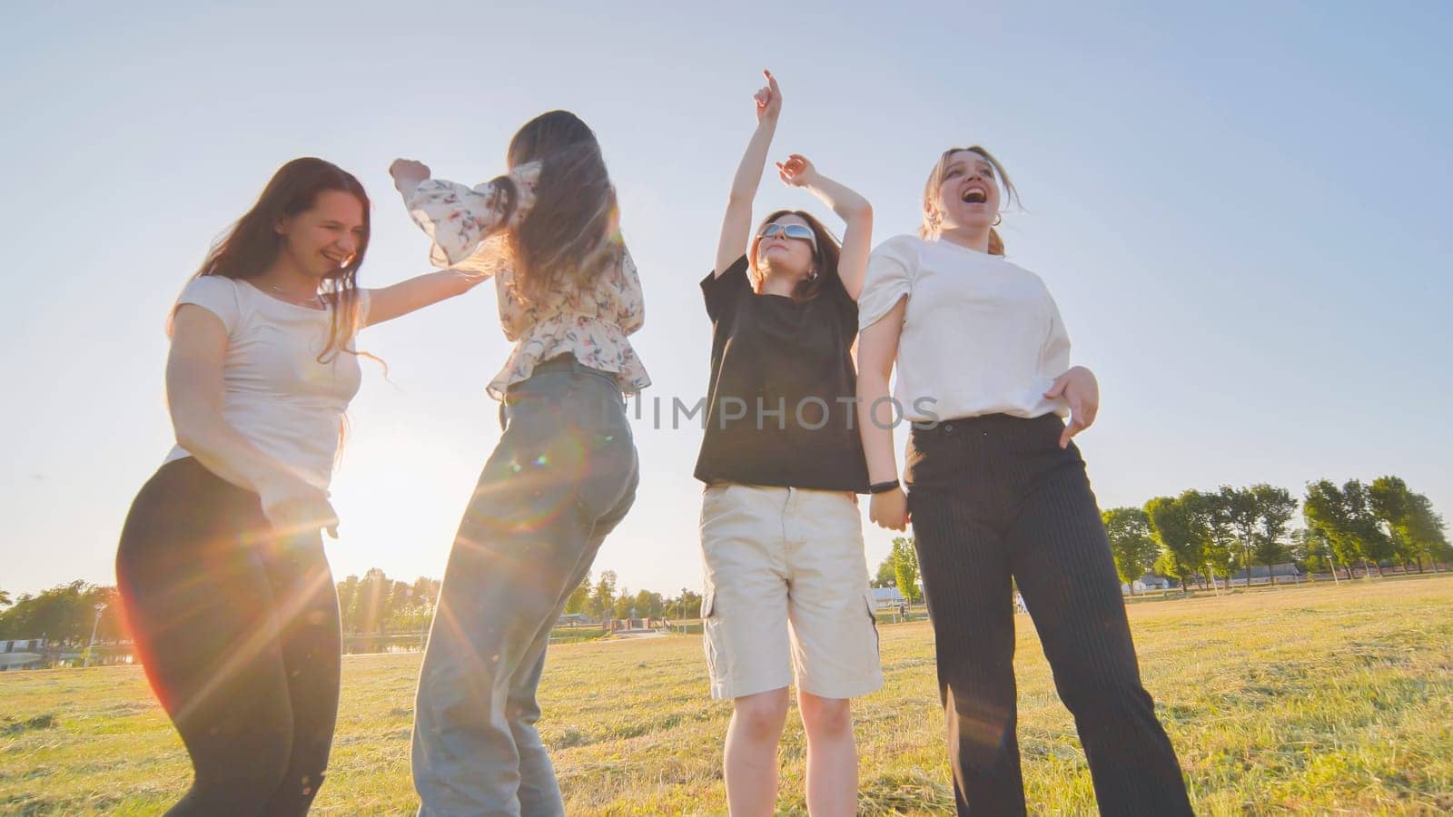 Funny jolly friends dancing in the city meadow in the evening