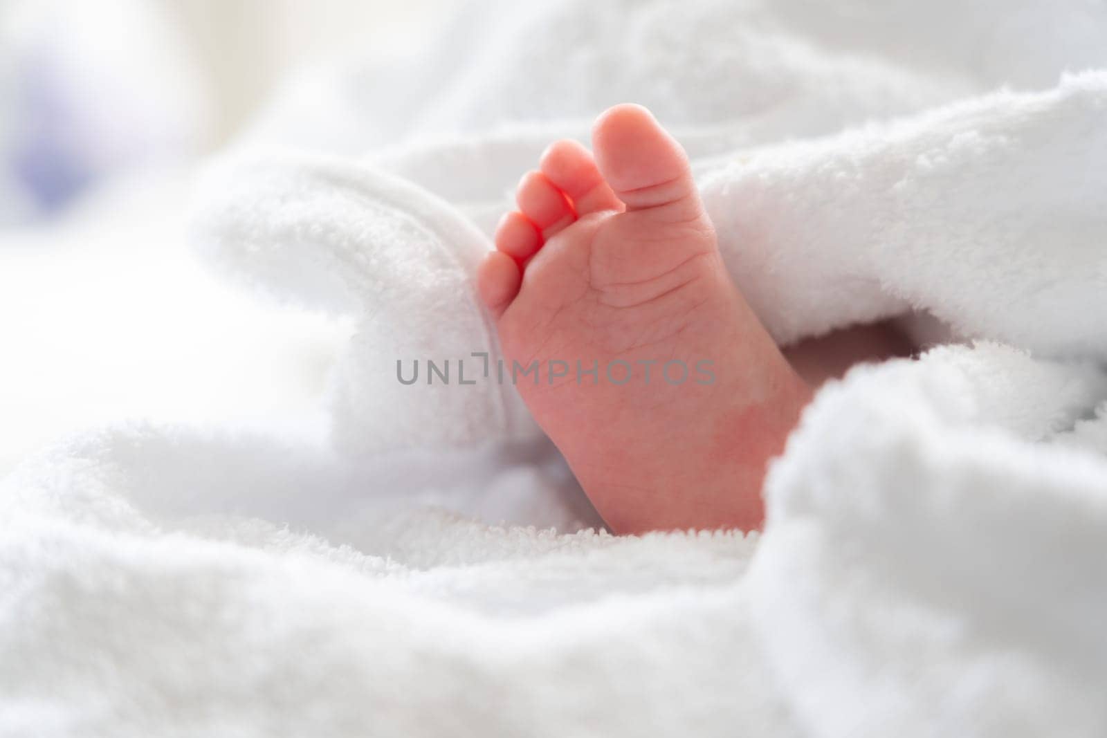 Following a soothing bath, the tiny foot of an infant peeks curiously from beneath a plush white towel, capturing a serene moment of newborn care