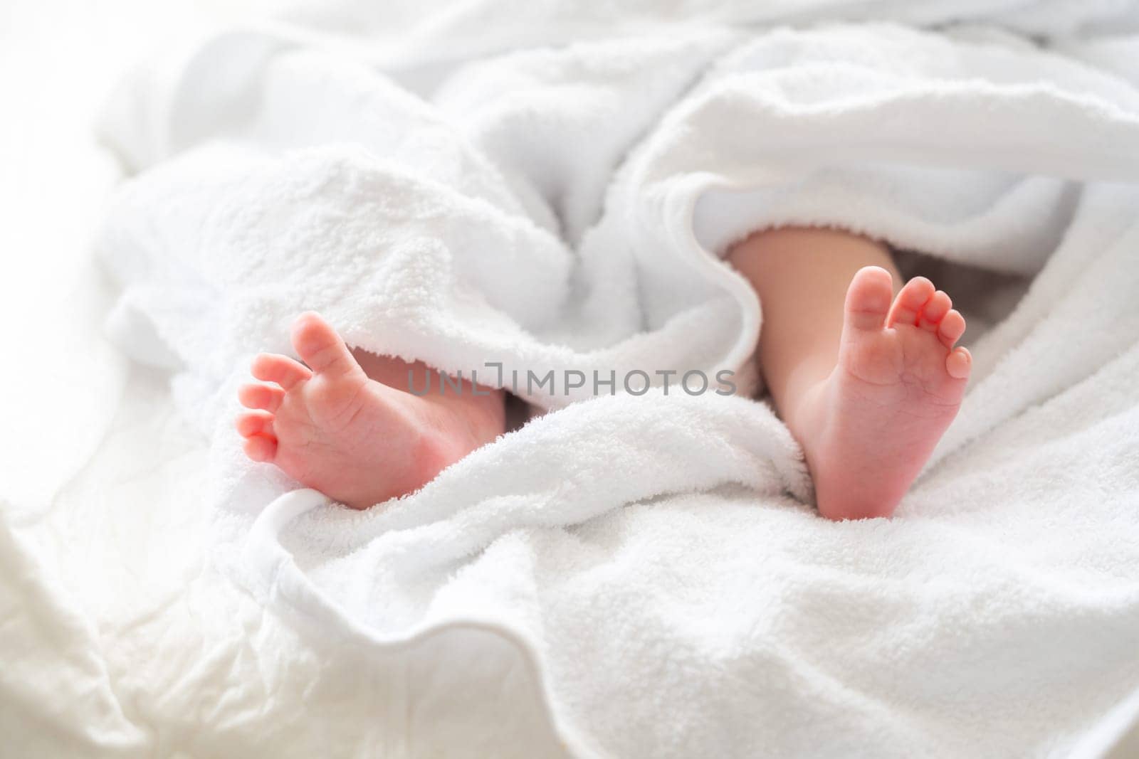 Newborn baby's feet delicately peeking from beneath a soft white towel capturing the essence of post-bath calmness and purity