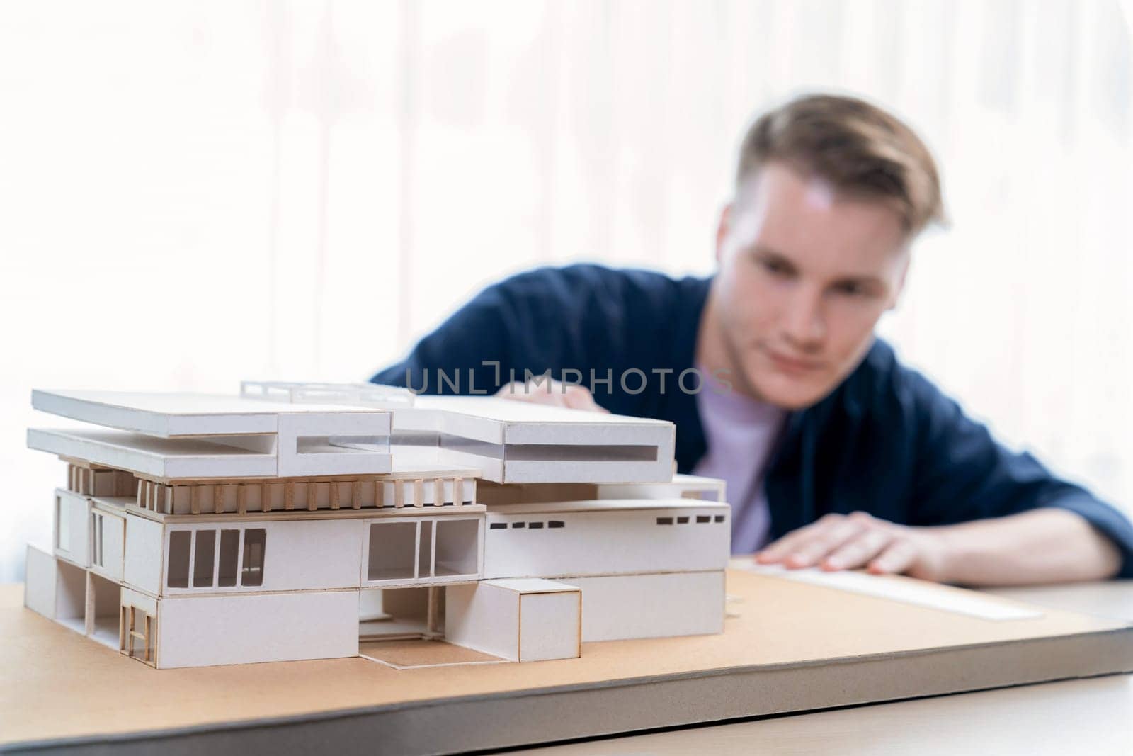 Architect designer studies elegant house model, reviewing structure design for improvement with construction plan on table. Creativity and innovation in architectural design. Iteration