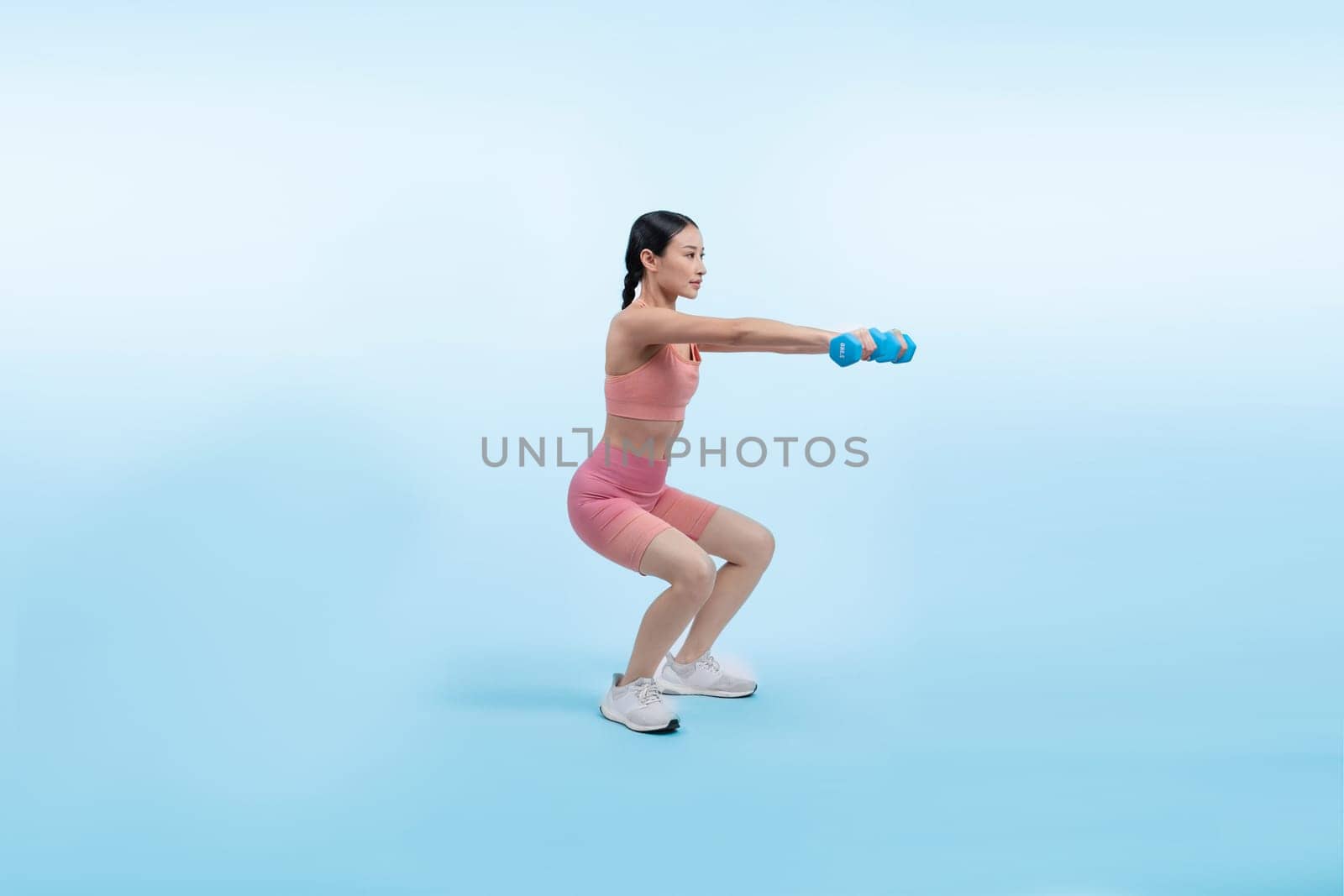 Vigorous energetic woman doing dumbbell weight lifting exercise on isolated background. Young athletic asian woman strength and endurance training session as body workout routine.