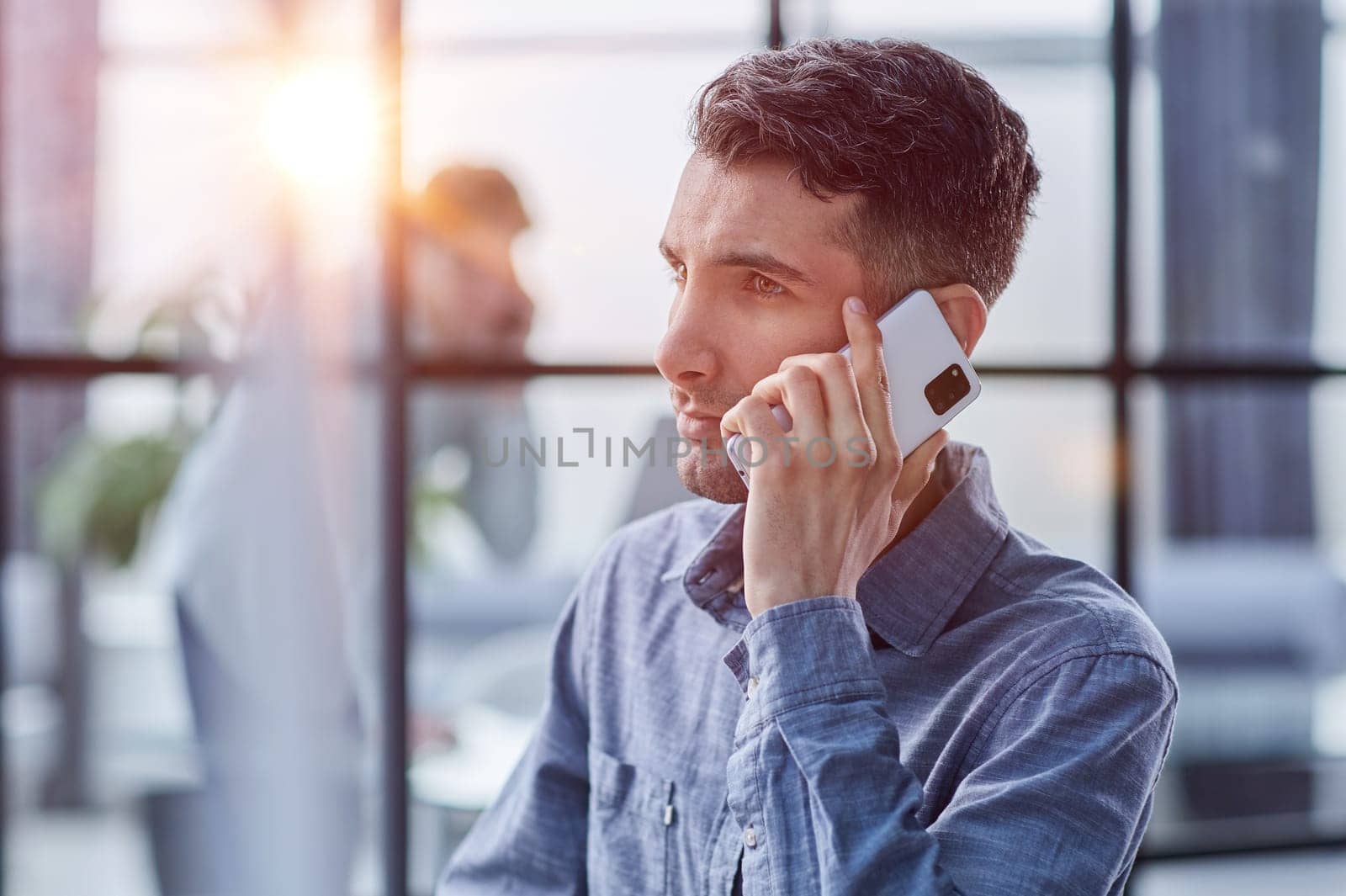 Portrait of young entrepreneur in casual office making phone call while working with laptop