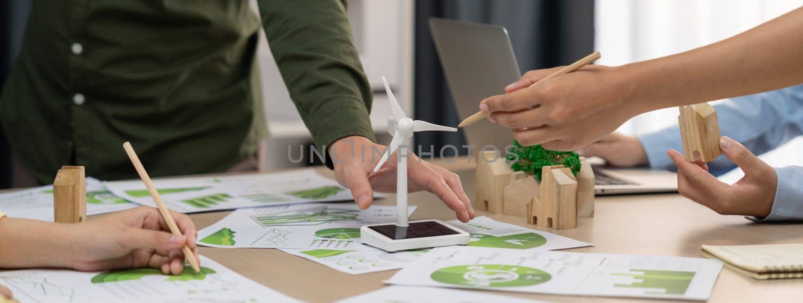 Windmill model represented renewable energy and wooden block represented eco city was placed on green business meeting table with environmental document scatter around. Front view. Delineation.