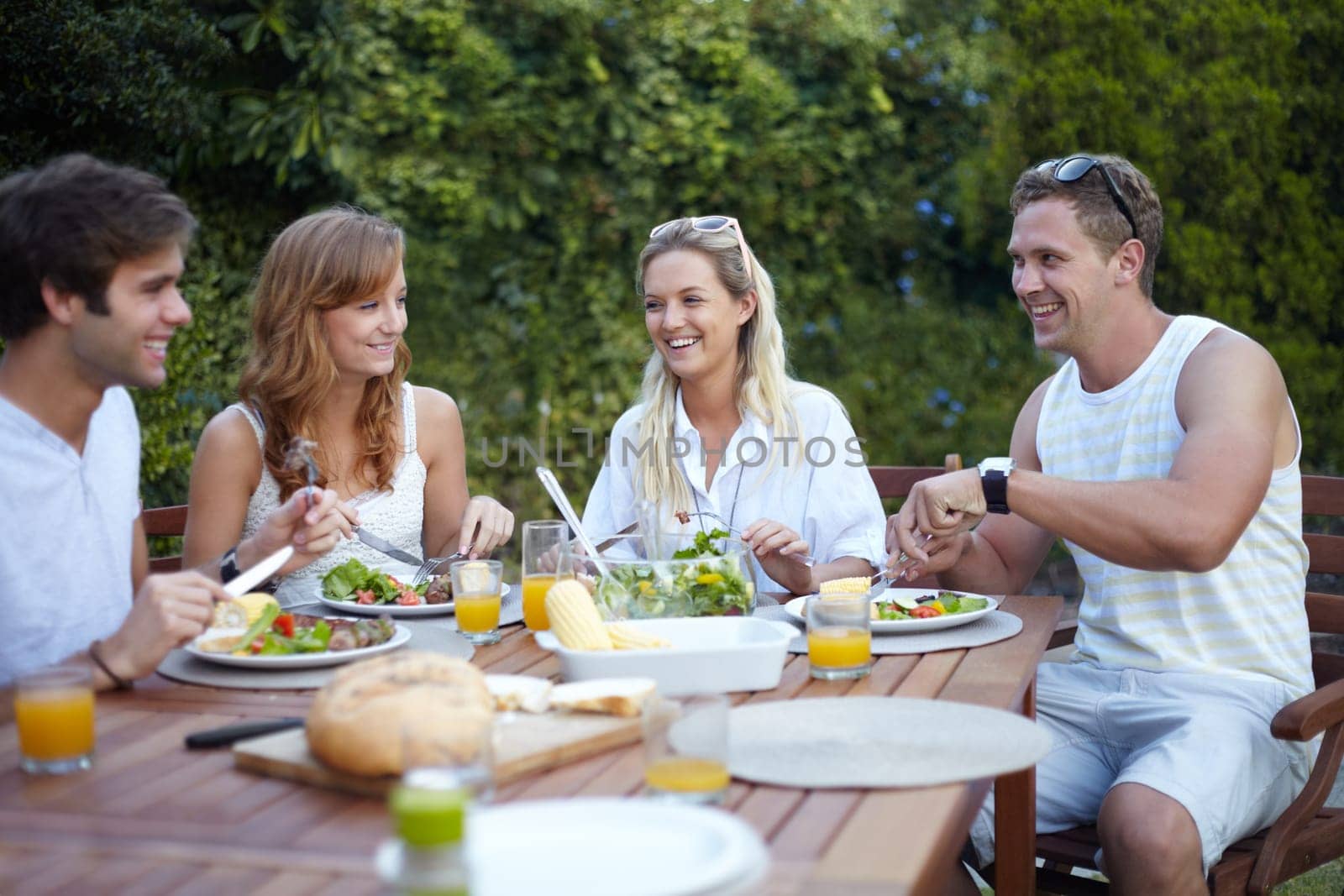 Friends, eating and healthy food in backyard for lunch and discussion with a smile with reunion. Salad, talking and young people outdoor of a home with conversation and relax dinner together by YuriArcurs