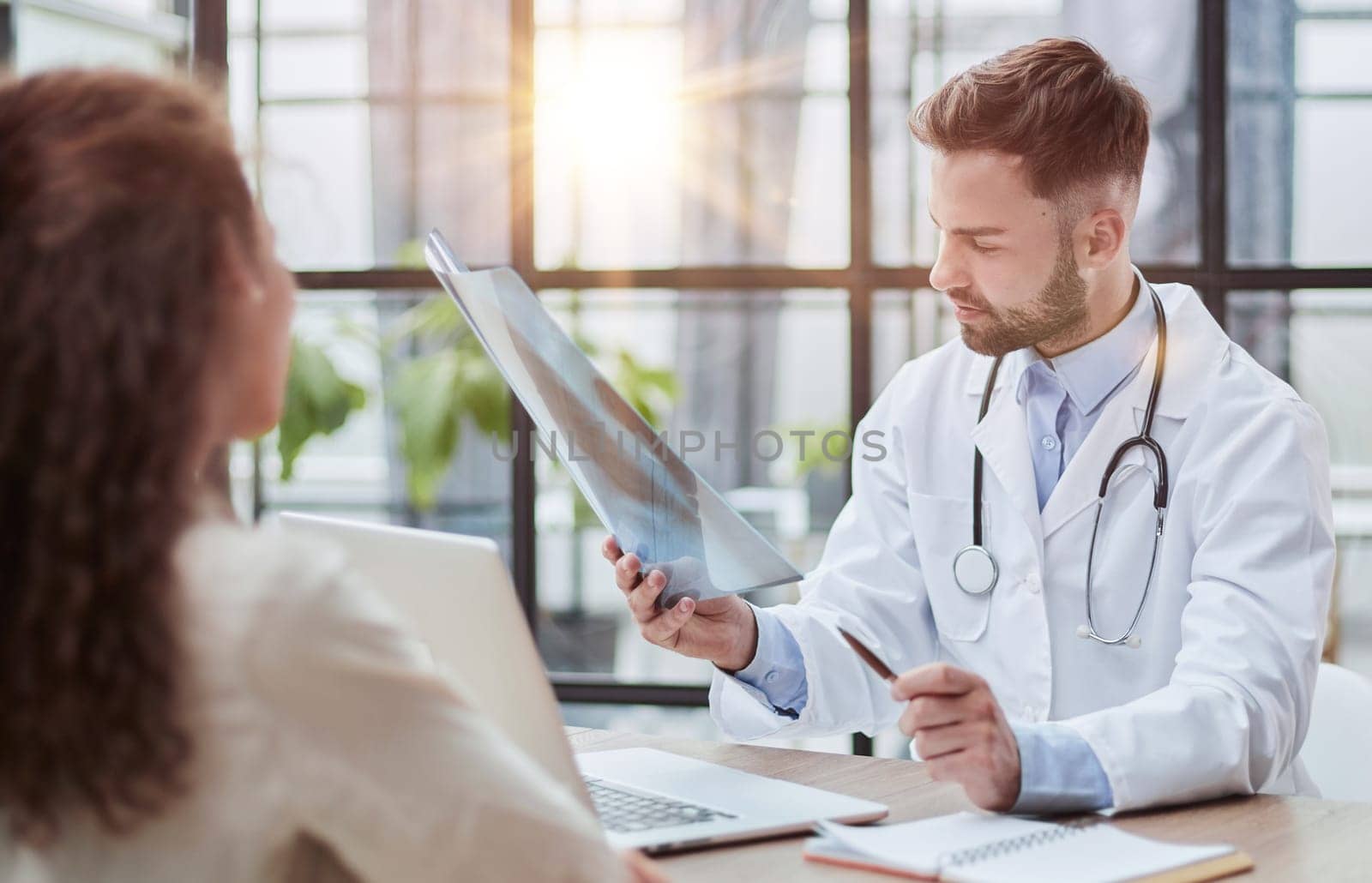 Young serious competent male doctor looking at X-ray at doctor's office