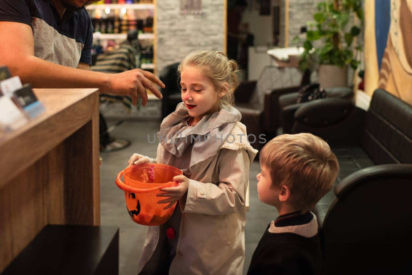 A man puts candy in a pumpkin-shaped bucket for Halloween. by Godi