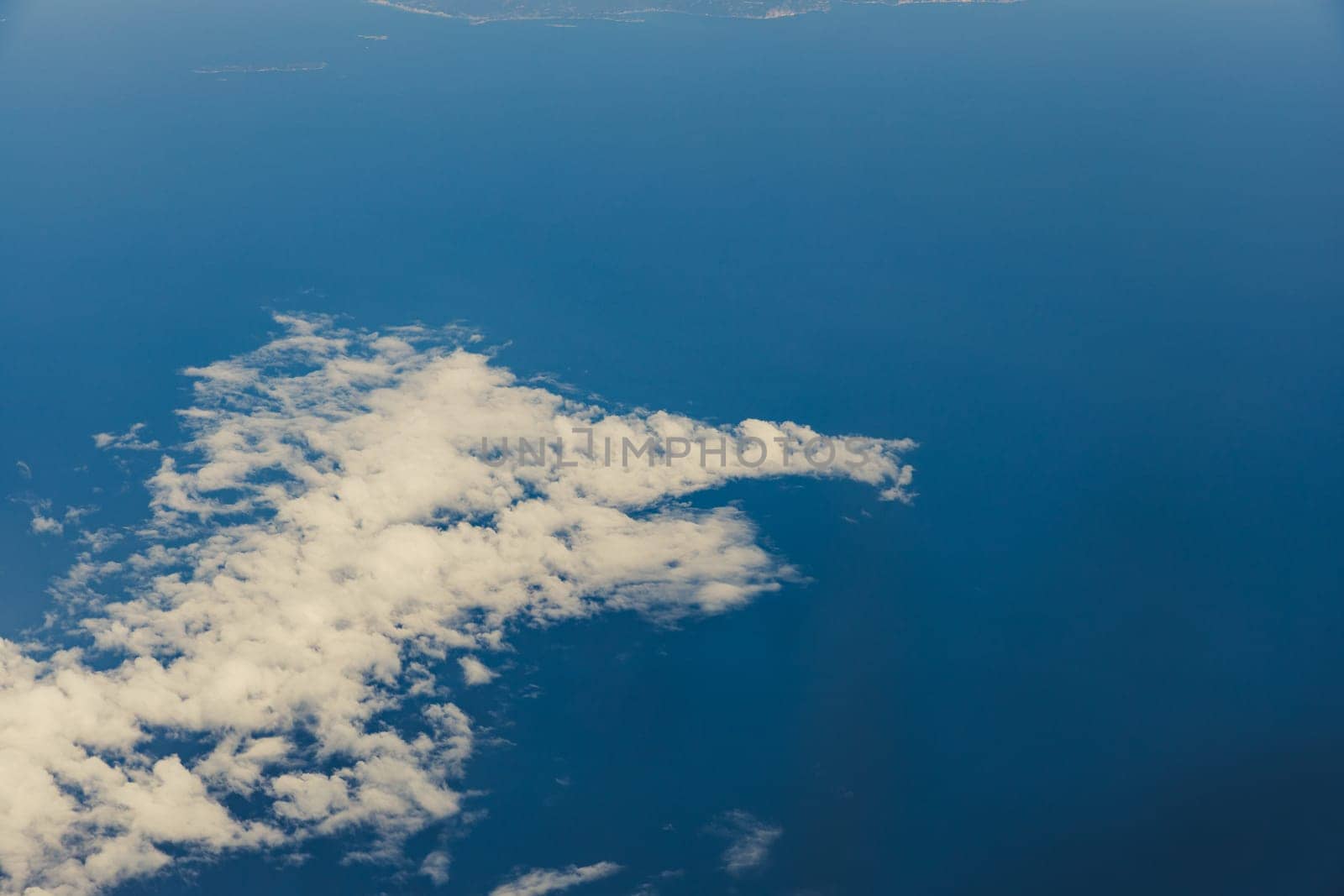 A beautiful view of a white cumulus cloud in the shape of a funny animal with a head and an open mouth through an airplane window in the summer during a flight, close-up side view.