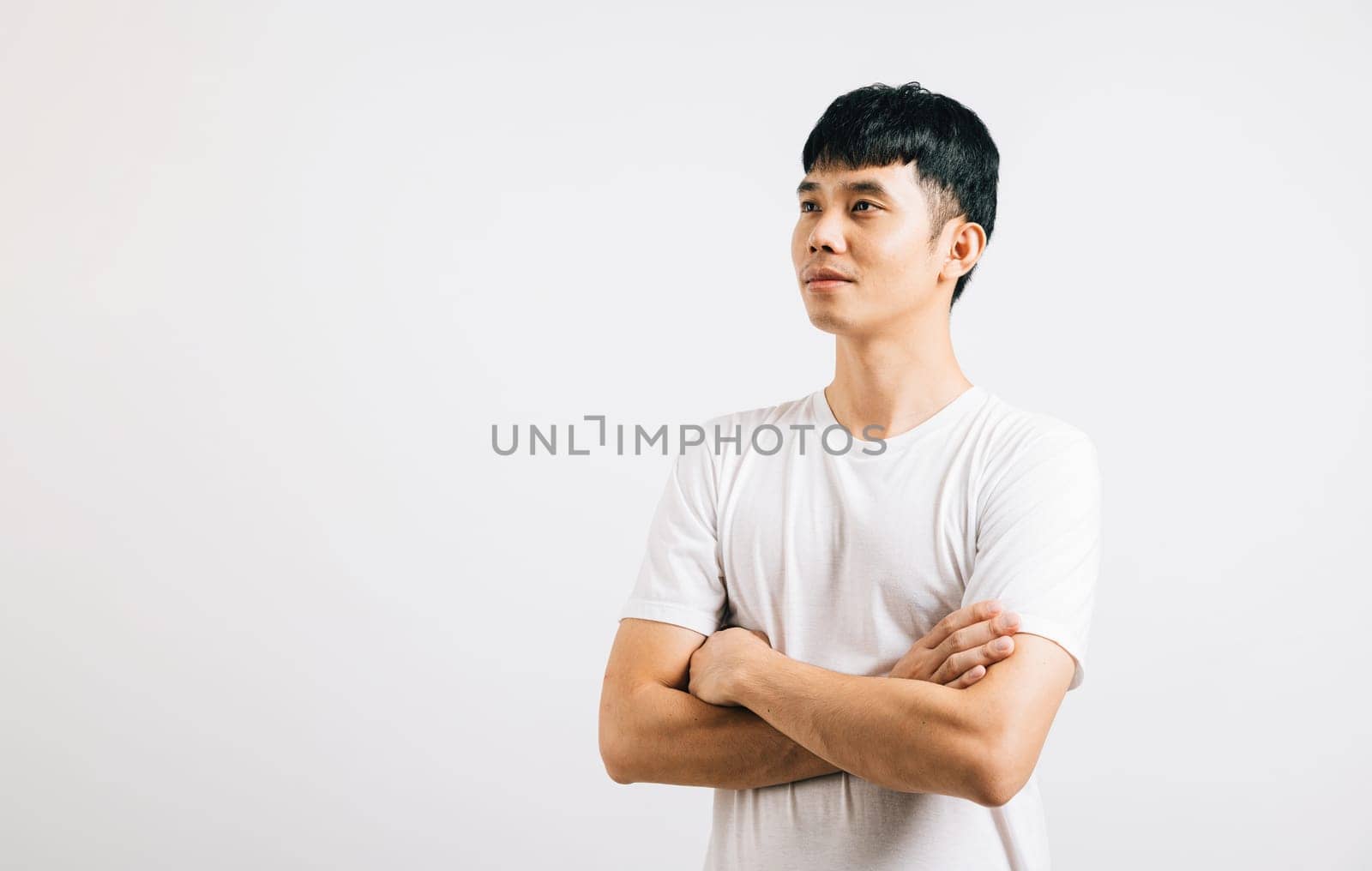 Portrait of a confident young Thai man with crossed arms, exuding success and a cheerful smile. Studio shot isolated on white background, radiating positivity.